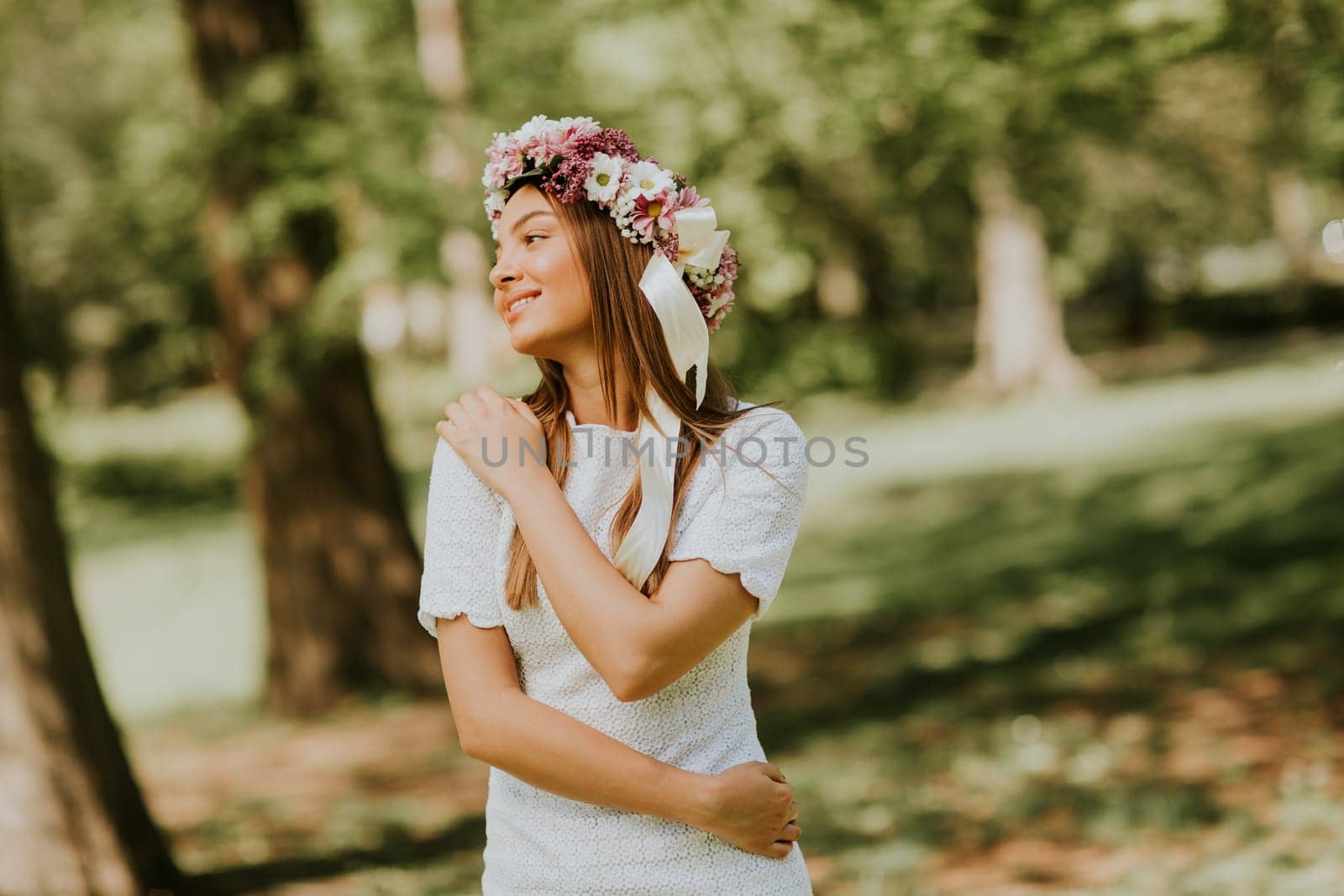 Portrait of young woman with wreath of fresh flowers on head in the park