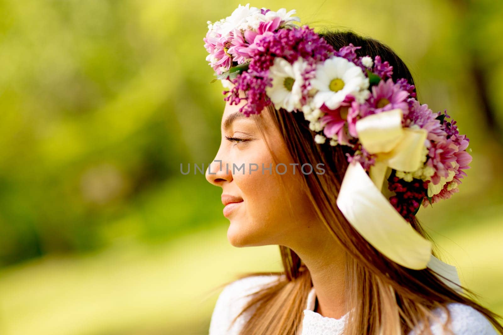Portrait of young woman with wreath of fresh flowers on head in the park
