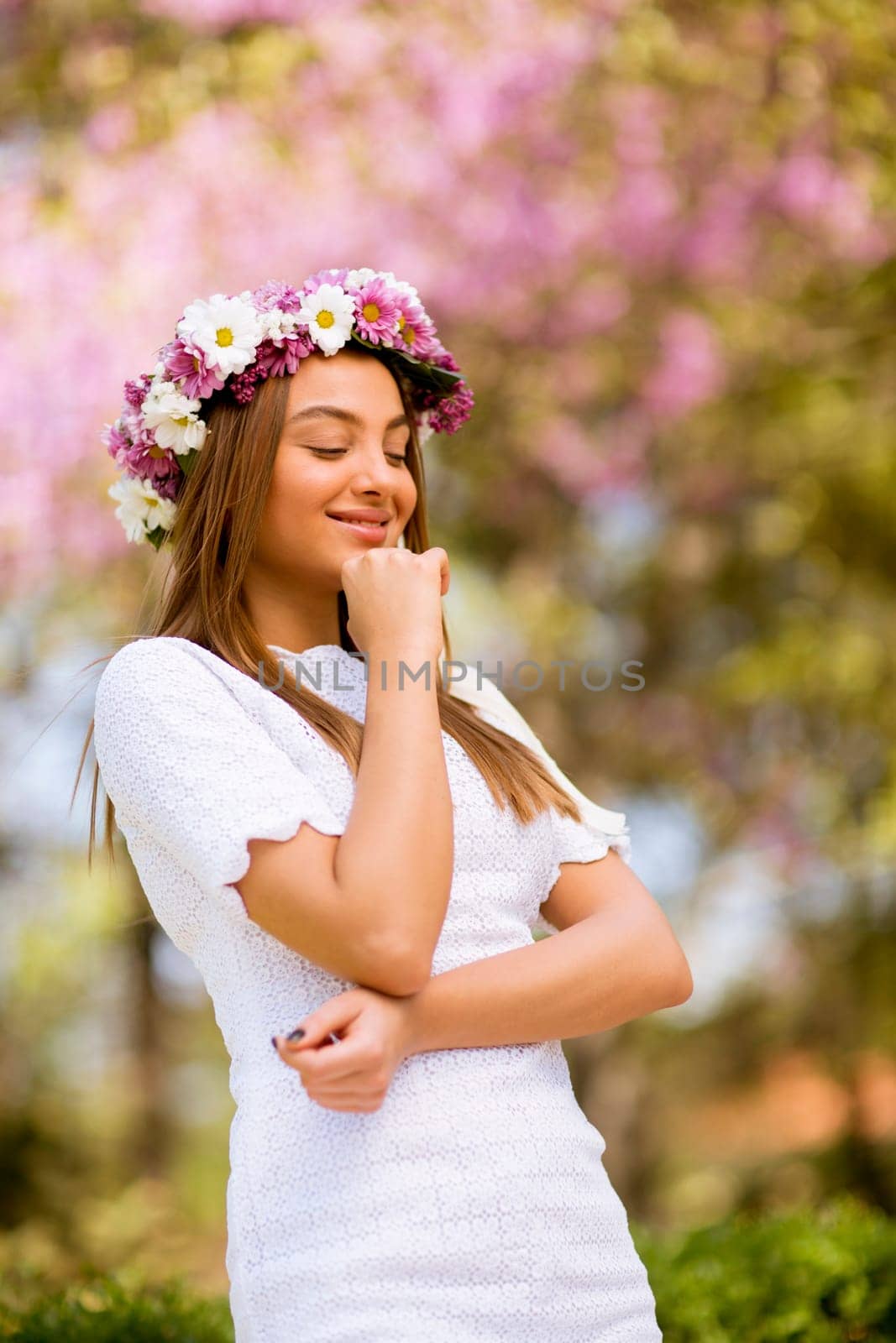 Portrait of pretty young woman with wreath of fresh flowers on head in the park