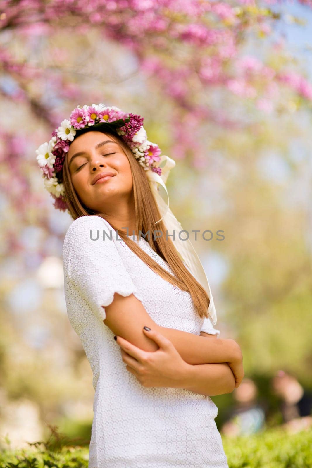 Portrait of pretty young woman with wreath of fresh flowers on head in the park