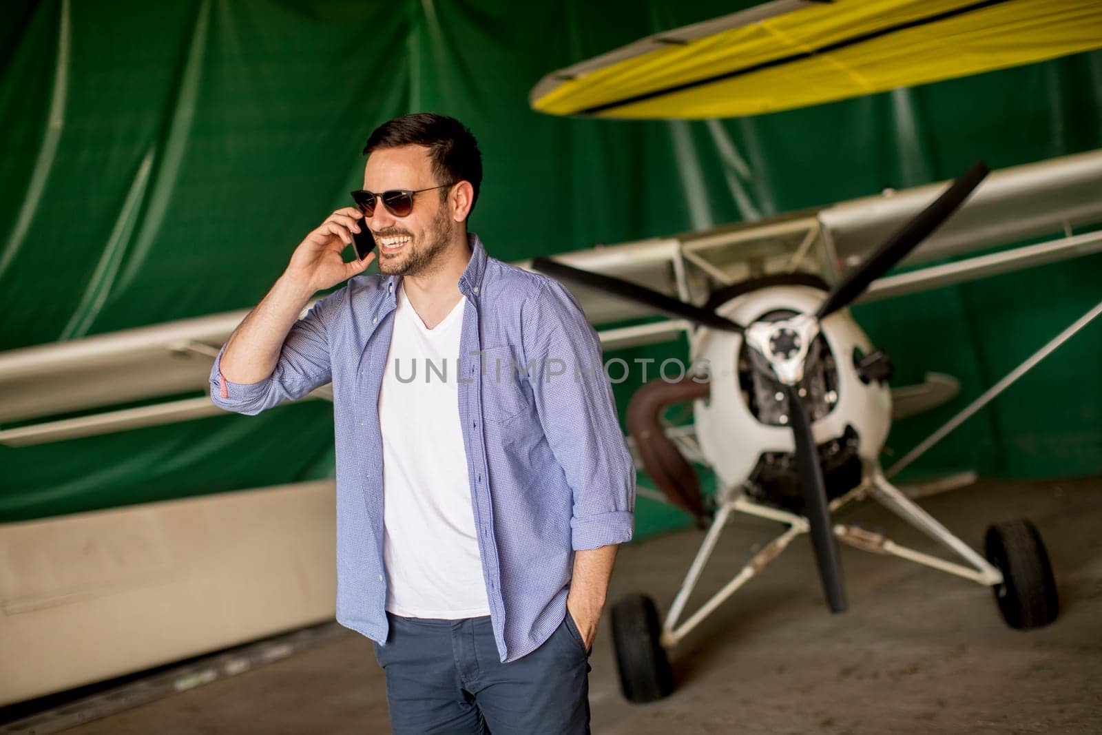 Handsome young man using mobile phone in the airplane hangar