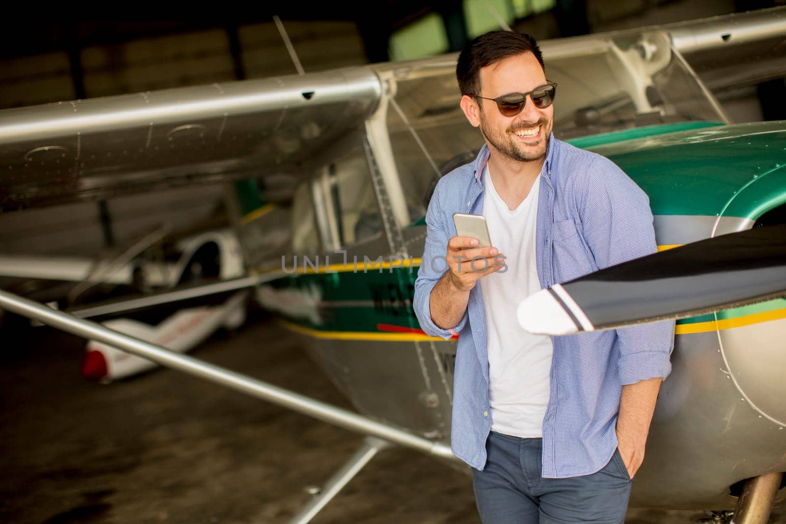 Handsome young man using mobile phone in the airplane hangar