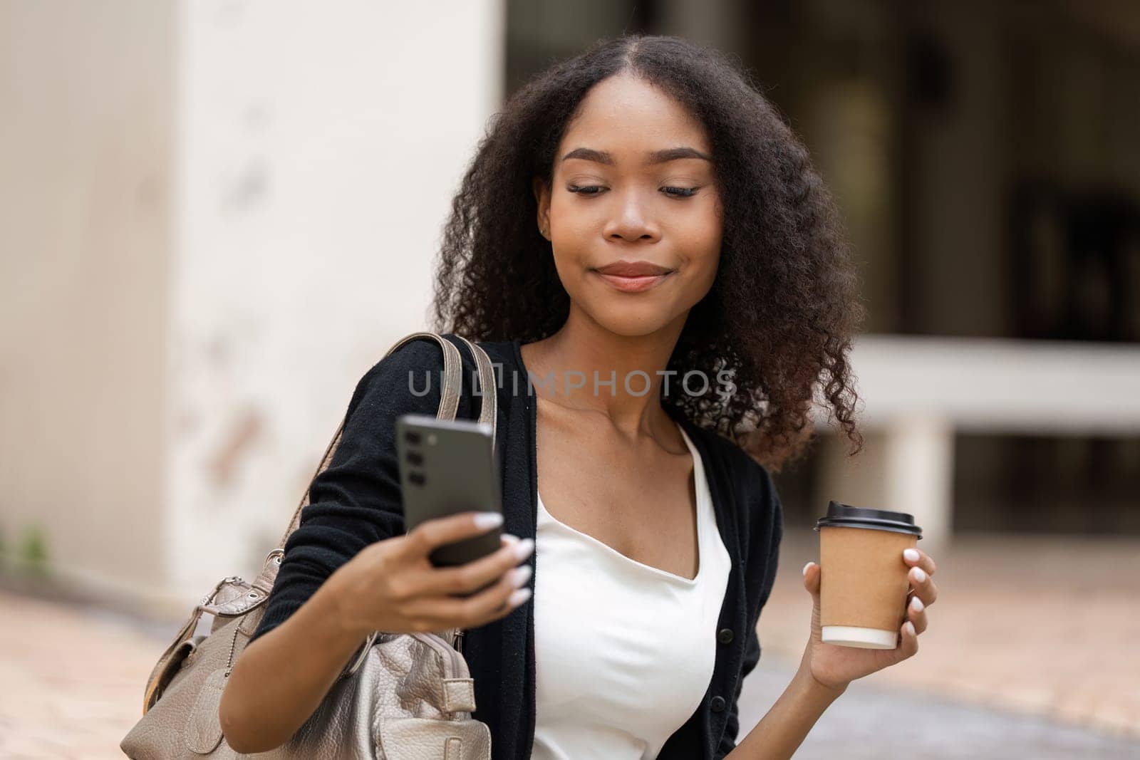 The young woman glances at her smartphone, coffee cup in hand, illustrating the blend of technology and casual living in her urbane lifestyle.