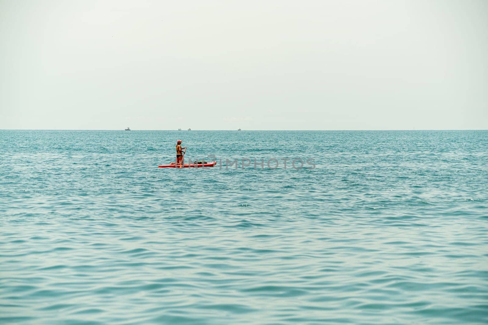 A person stands on a paddleboard, navigating through tranquil sea waters. The sky is overcast, creating a peaceful atmosphere as they enjoy a leisurely outing on the water.