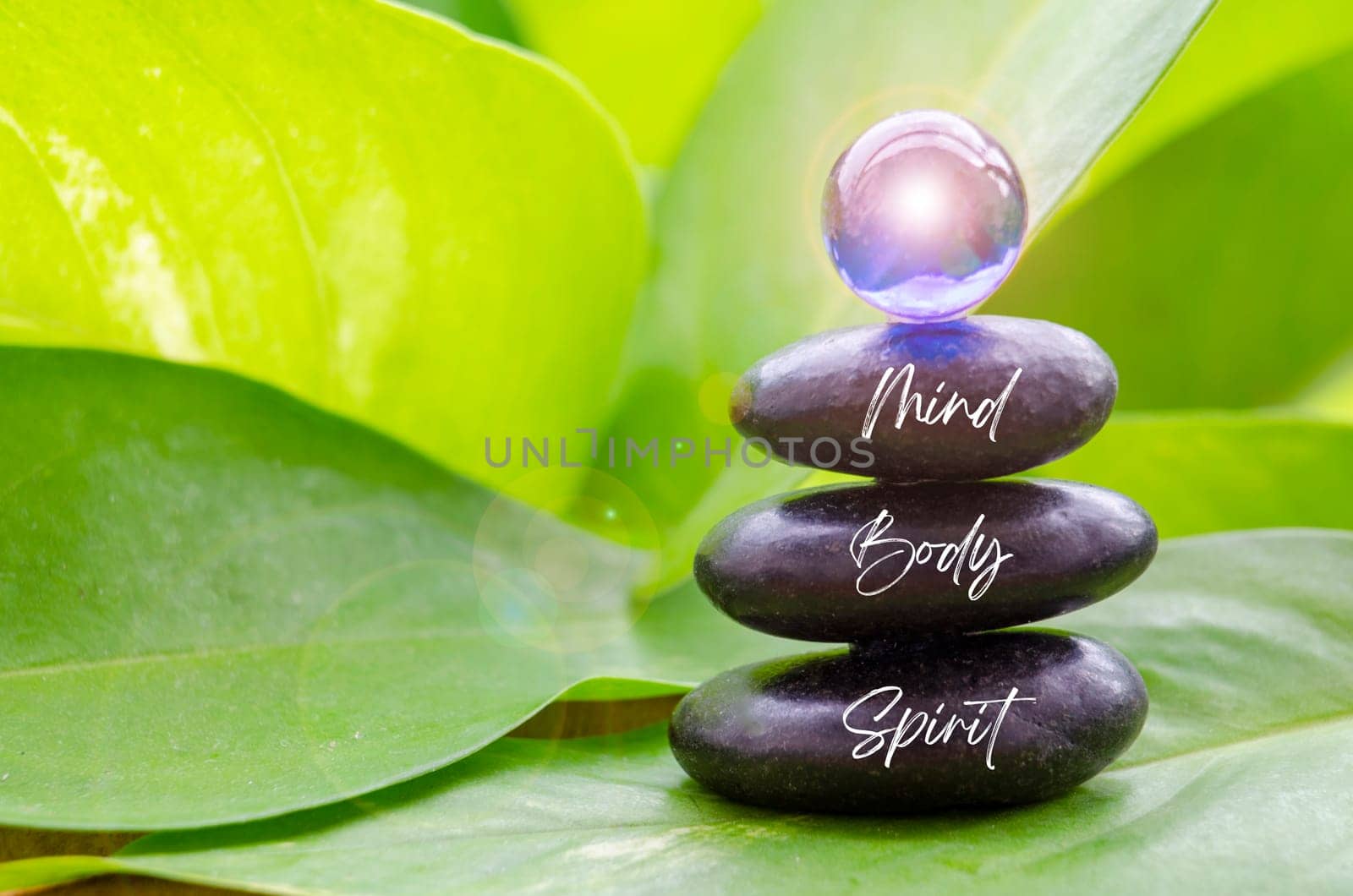 Mind, Body and Spirit text on black zen stones with blue shining glass marble on top. Zen concept.