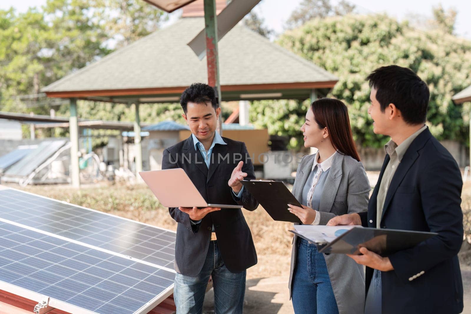 A engaged team discussing the use of solar panels and its benefits for business sustainability efforts outdoors.