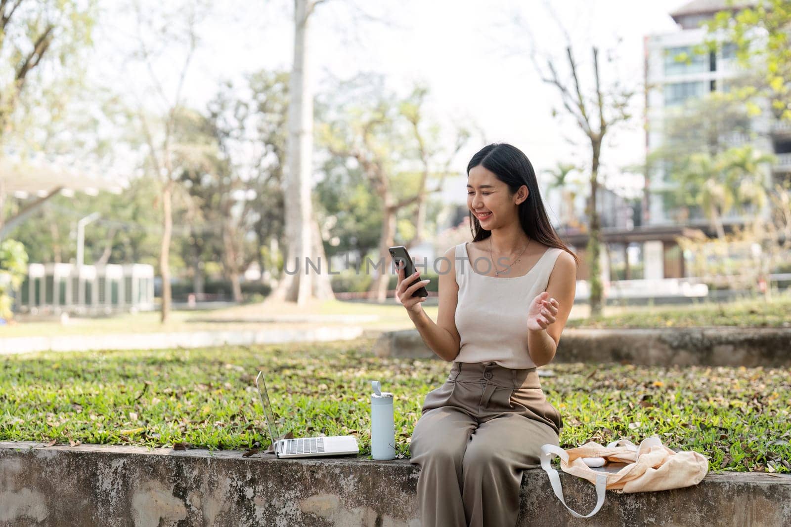 A young woman smiles while using her smartphone in a green park, reflecting a sustainable lifestyle and connection with nature.