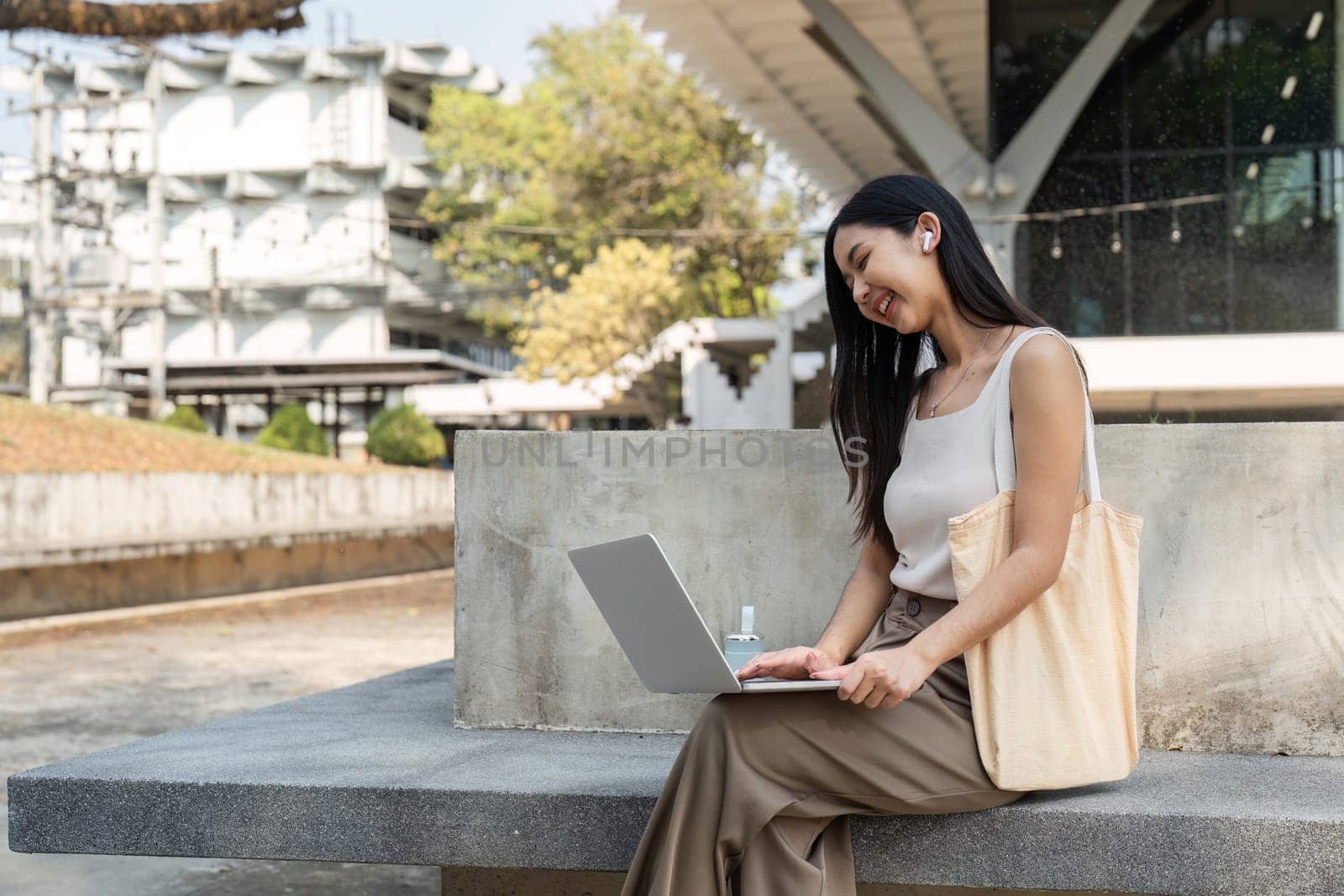 A young woman engages with her laptop in a modern outdoor setting, embodying a sustainable lifestyle while working.