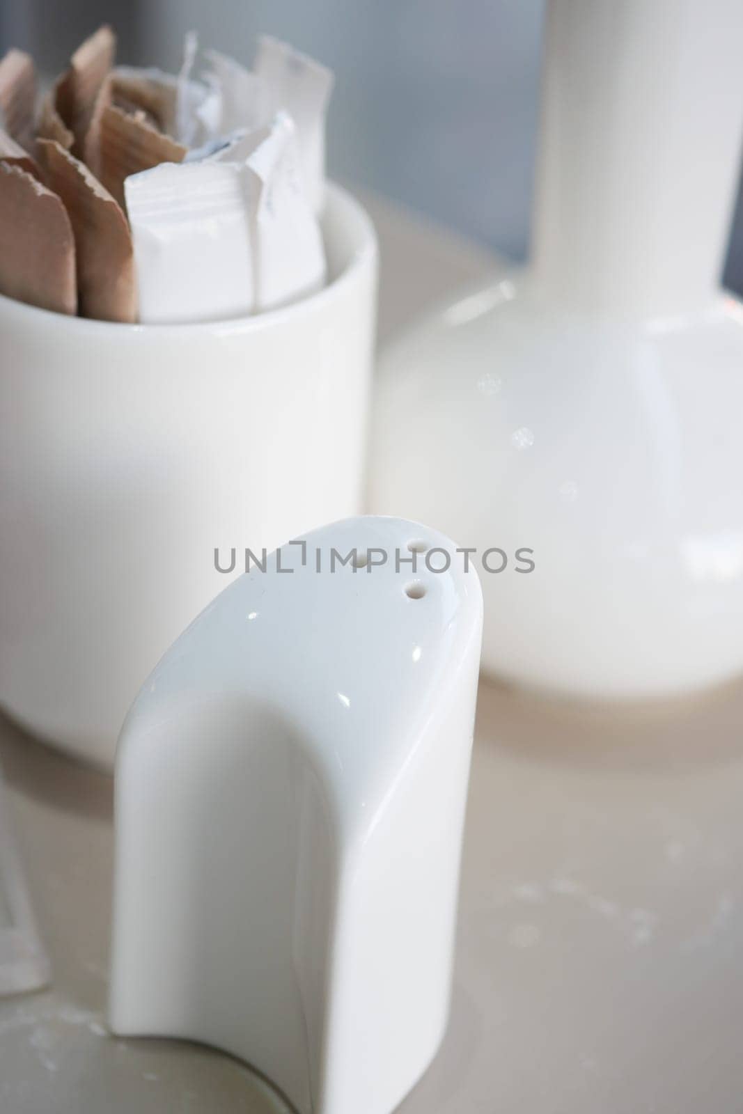 A white salt shaker sits beside sugar packets in a modern setting.