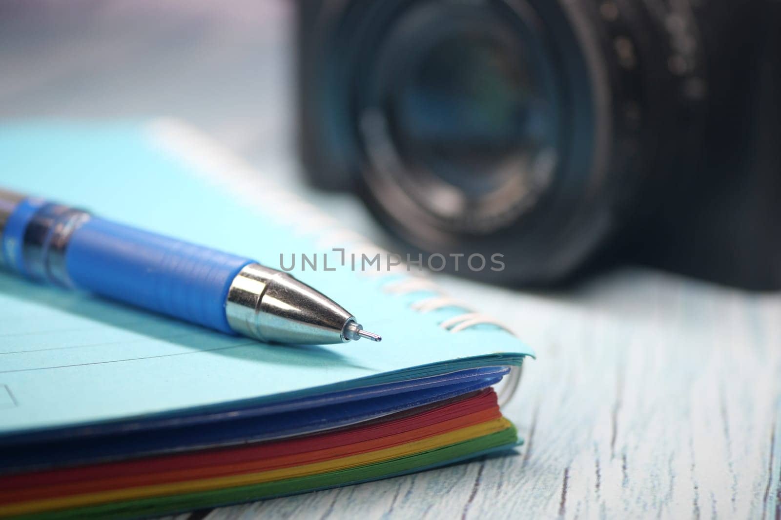 A colorful notebook and pen are placed near a camera on a desk.