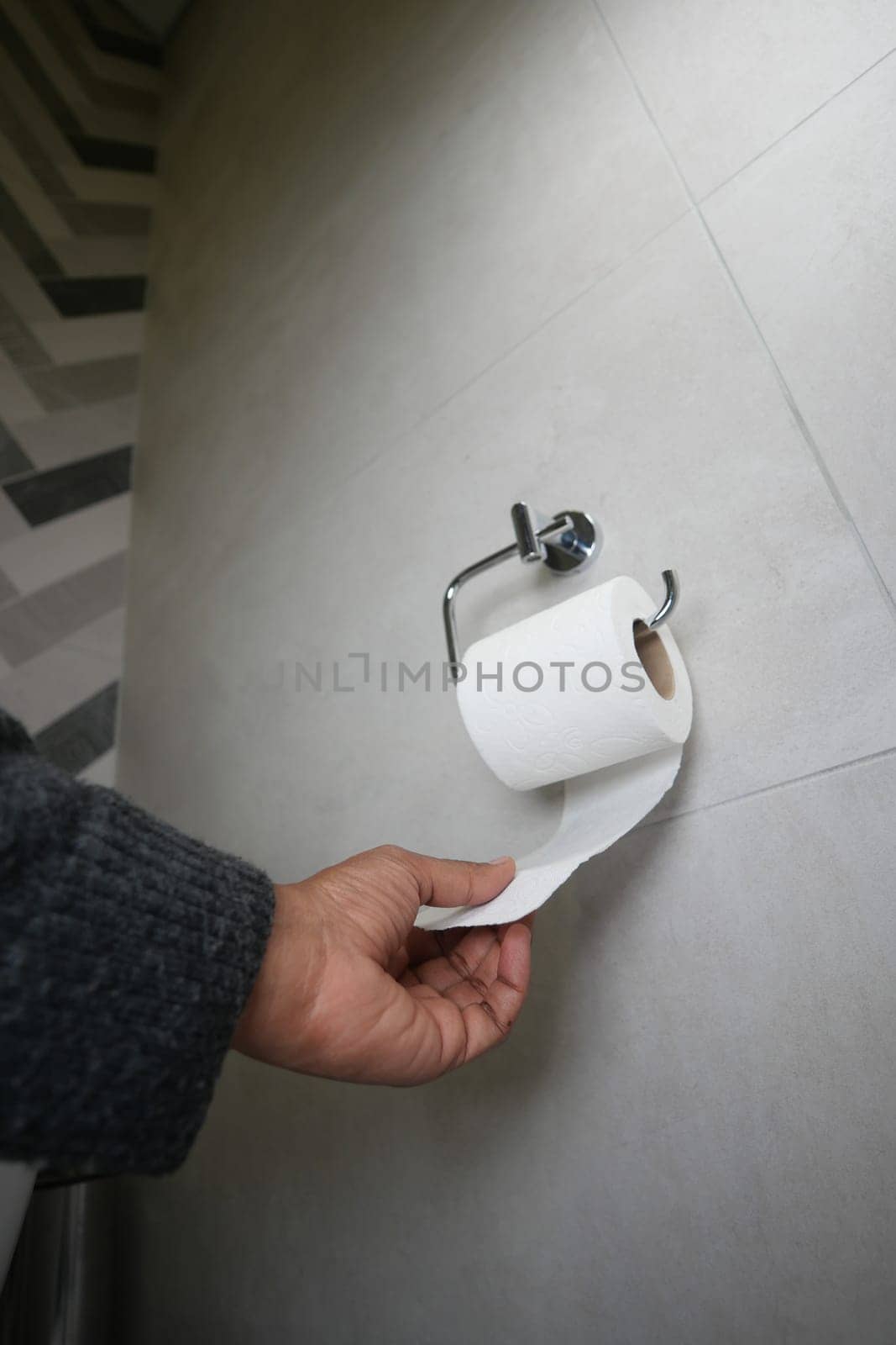 A hand is pulling down toilet paper from a roll in a stylish restroom.