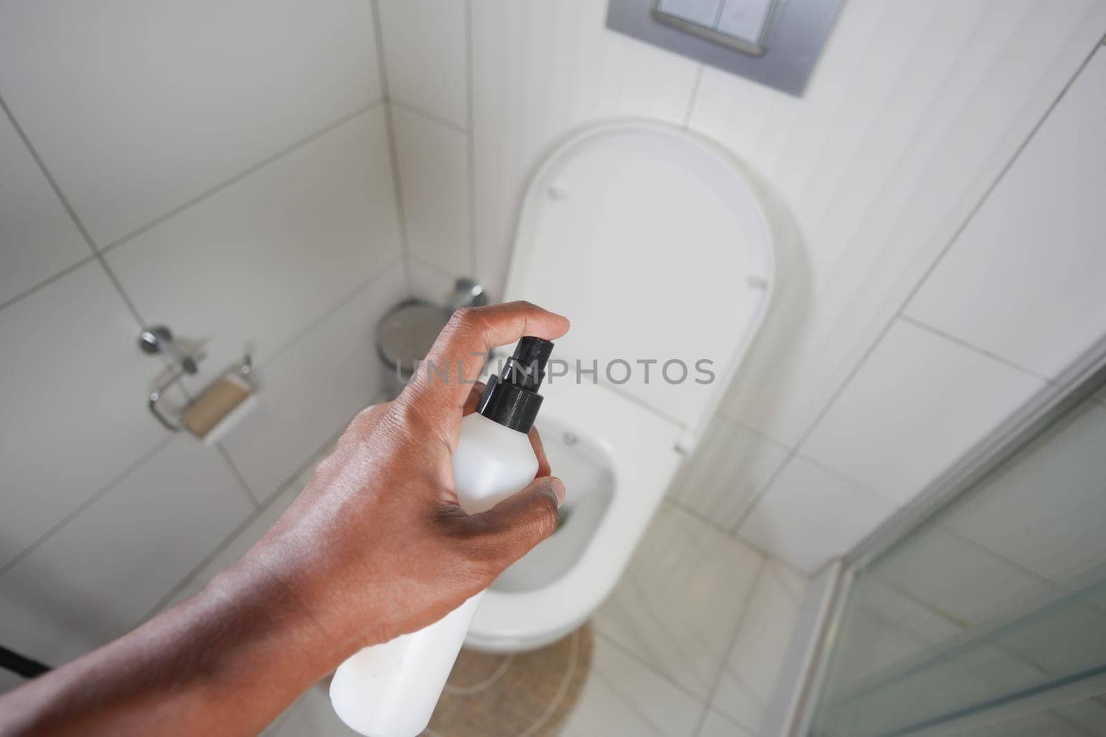 Person applying cleaning solution to a toilet in a tidy bathroom.