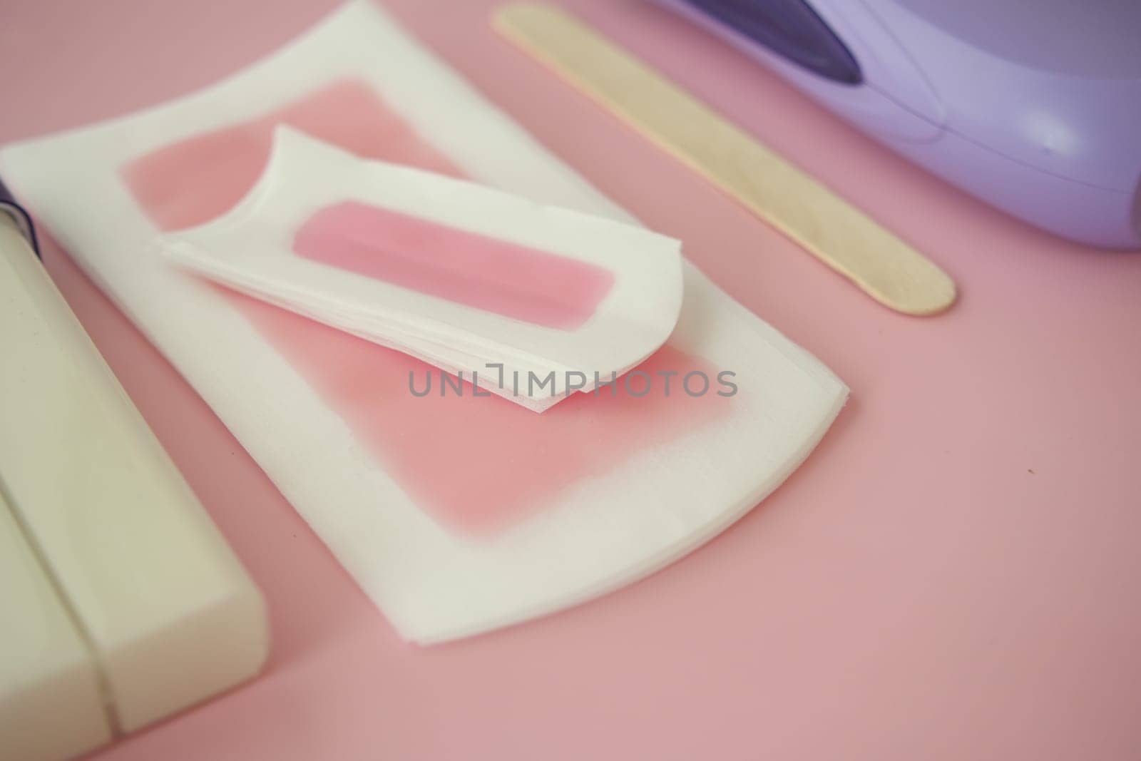 Various waxing supplies laid out neatly on a soft pink surface.