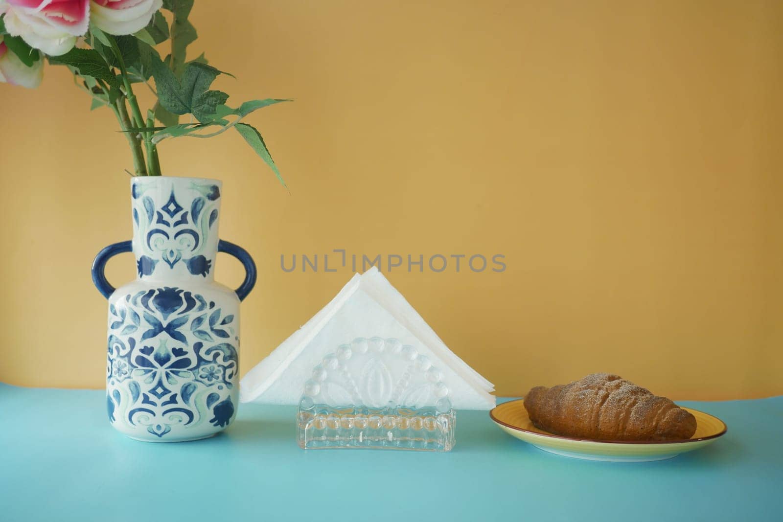 A cheerful breakfast table with flowers, a croissant, and napkins.