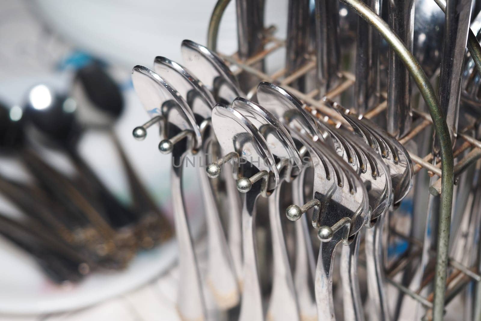 Shiny cutlery drying on a rack after being washed in the kitchen.