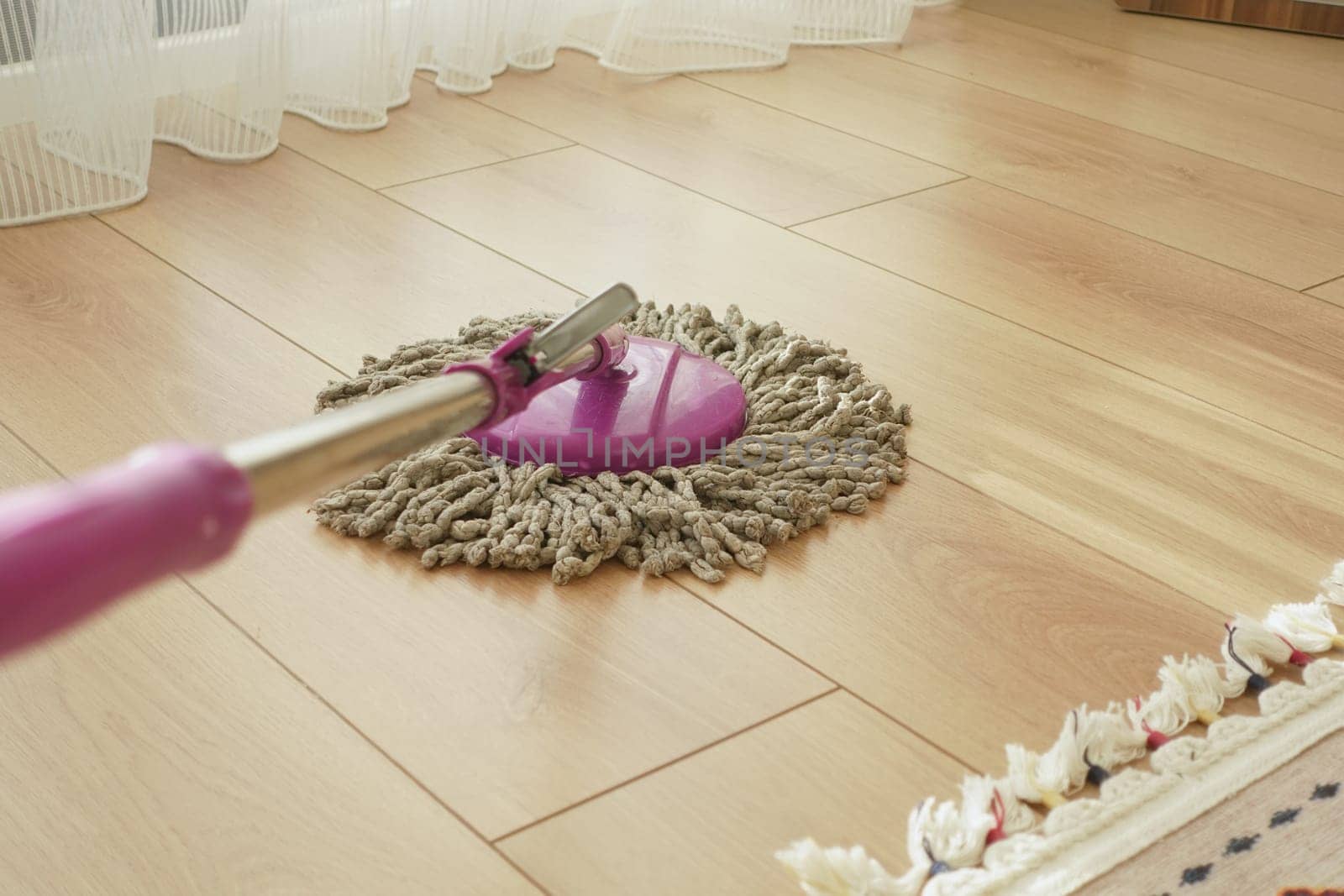 A person mops a wooden floor in a well-lit space with sunlight.