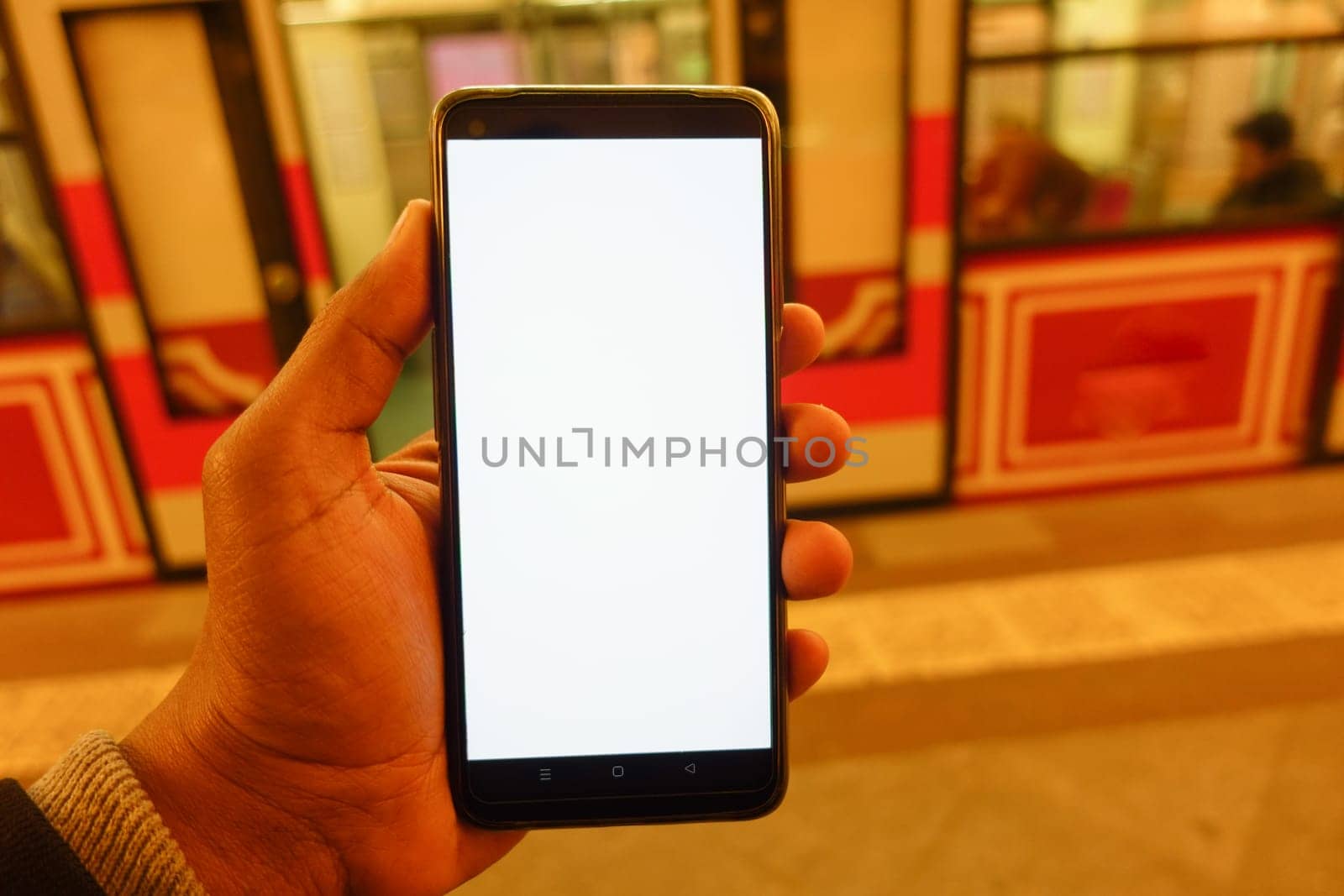 Individual displays a blank smartphone while waiting for train arrival.