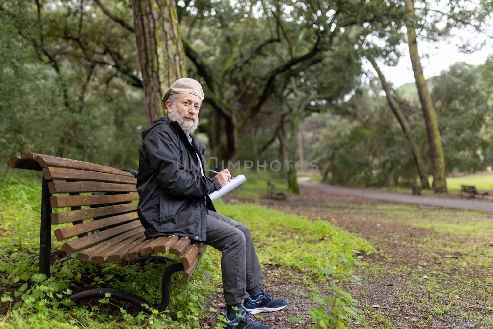 Elderly man writing notes while sitting on bench in a tranquil park