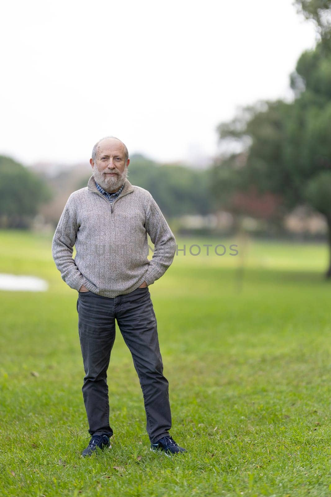 Portrait of a content senior man standing in a green park, enjoying his retirement