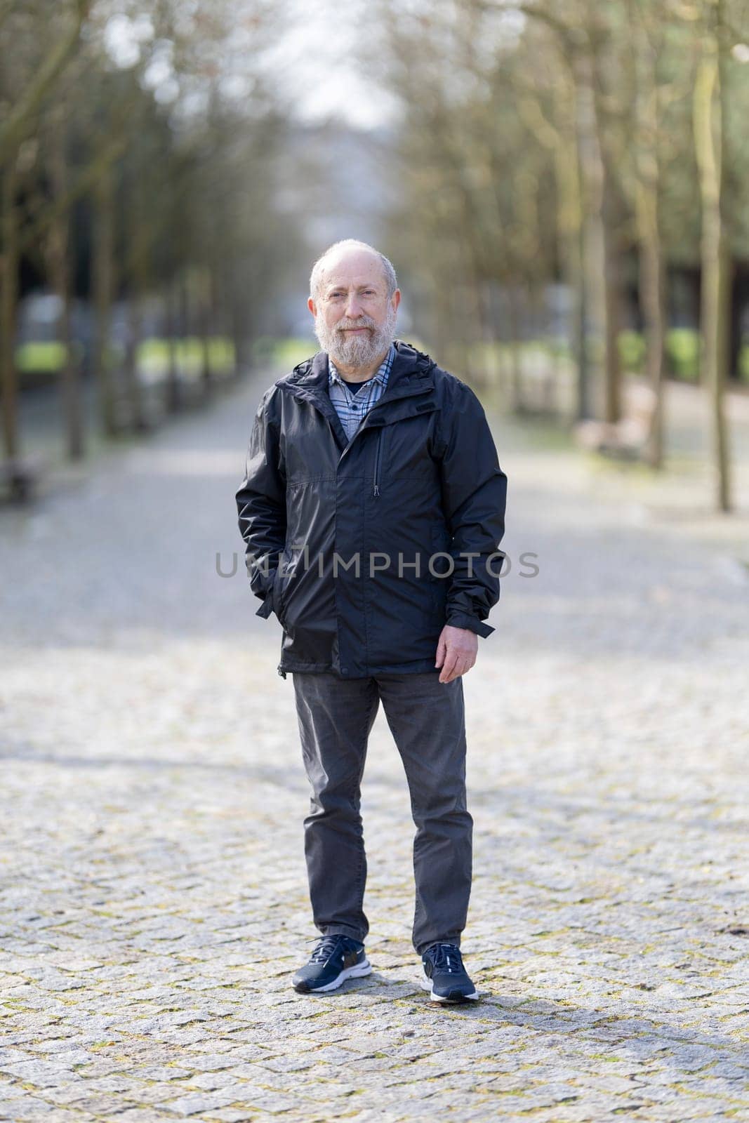 Portrait of a confident senior man standing on a paved path in a park, enjoying the fresh air and tranquility of nature