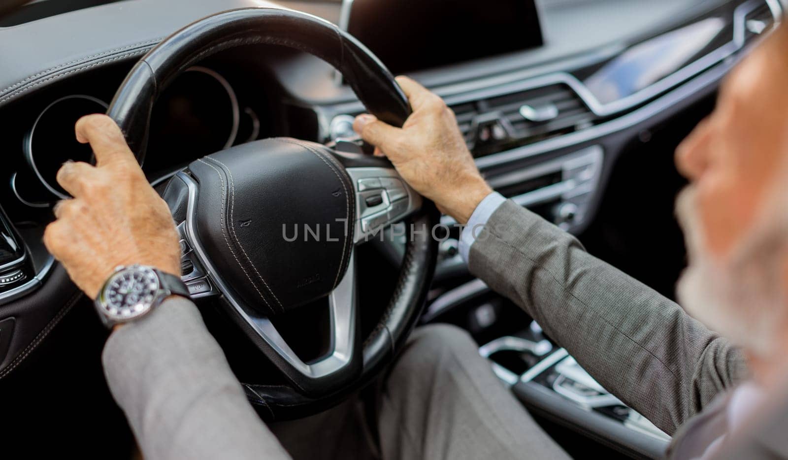 Cheerful elderly man in a suit driving leisurely, basking in the warm glow of a bright day