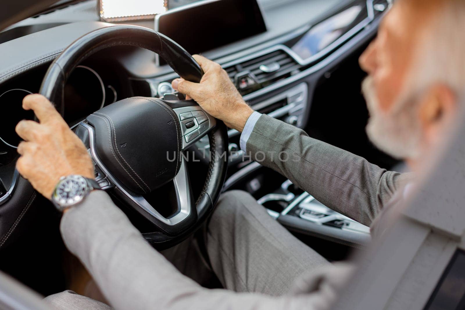 Cheerful elderly man in a suit driving leisurely, basking in the warm glow of a bright day