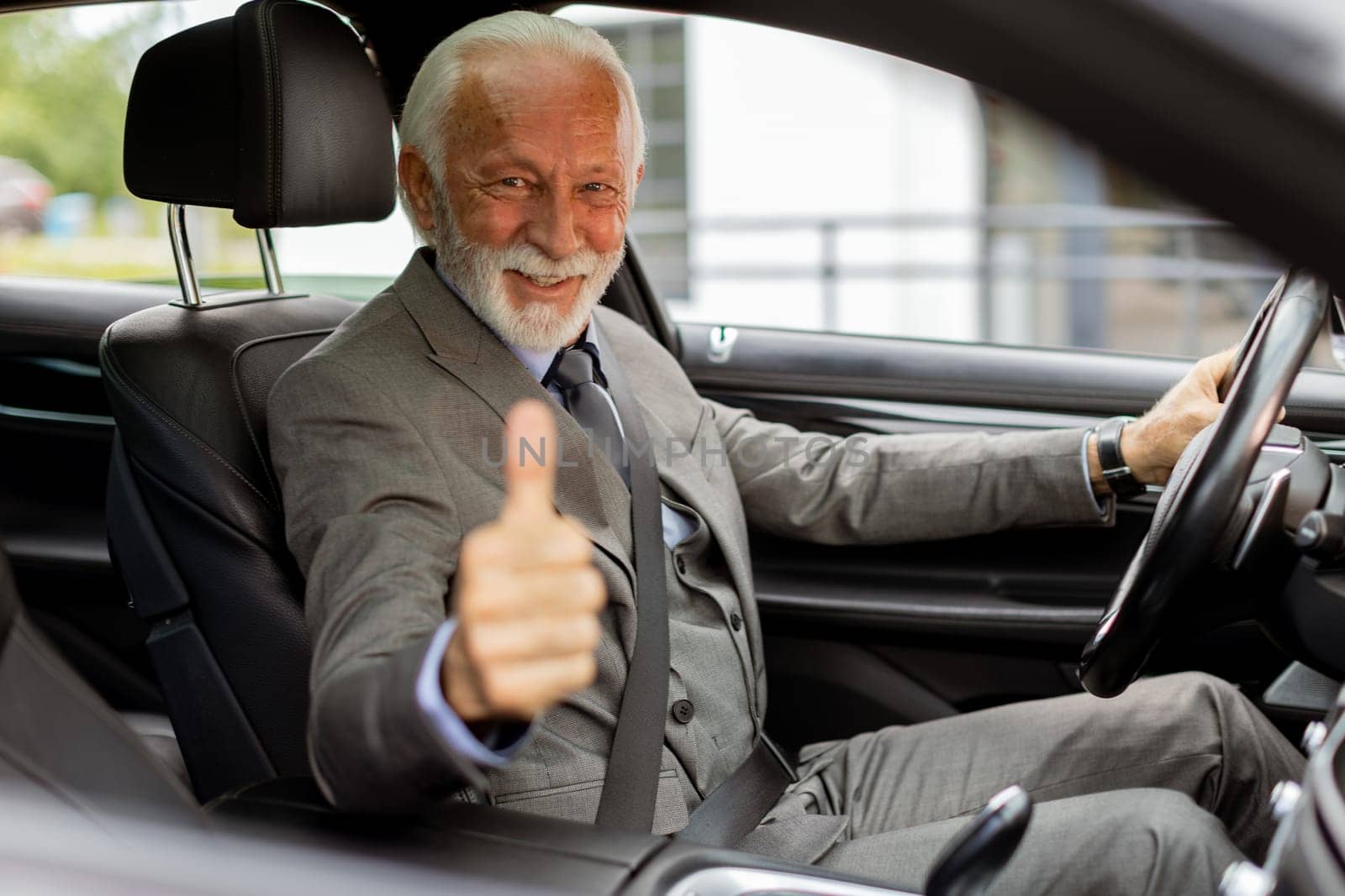 An elderly man in a suit smiles with approval from the drivers seat