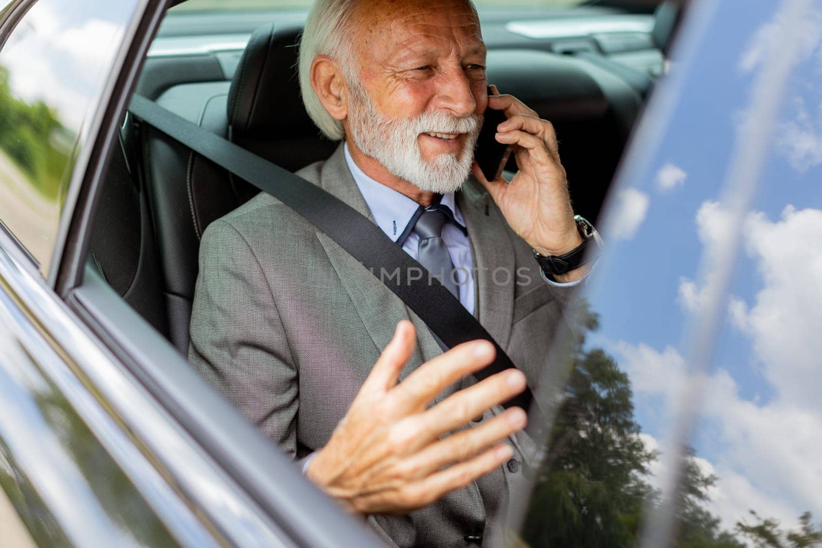 Suave senior man converses on his cell during a leisurely car ride, exuding charm and confidence