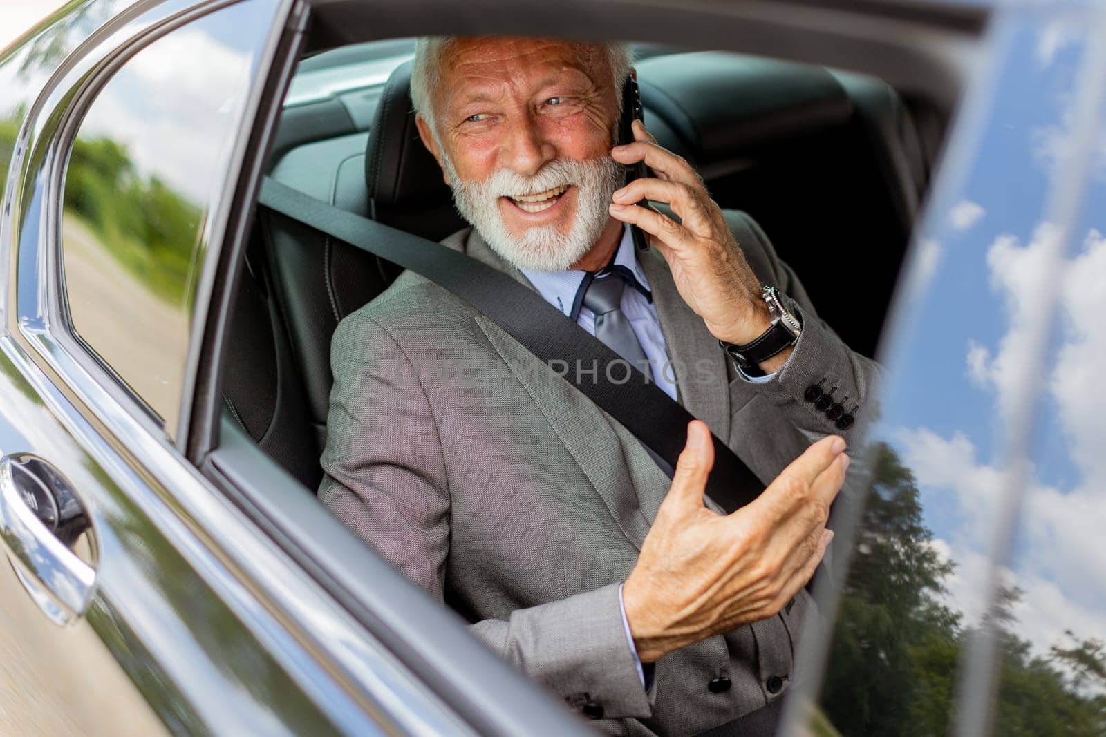 Suave senior man converses on his cell during a leisurely car ride, exuding charm and confidence
