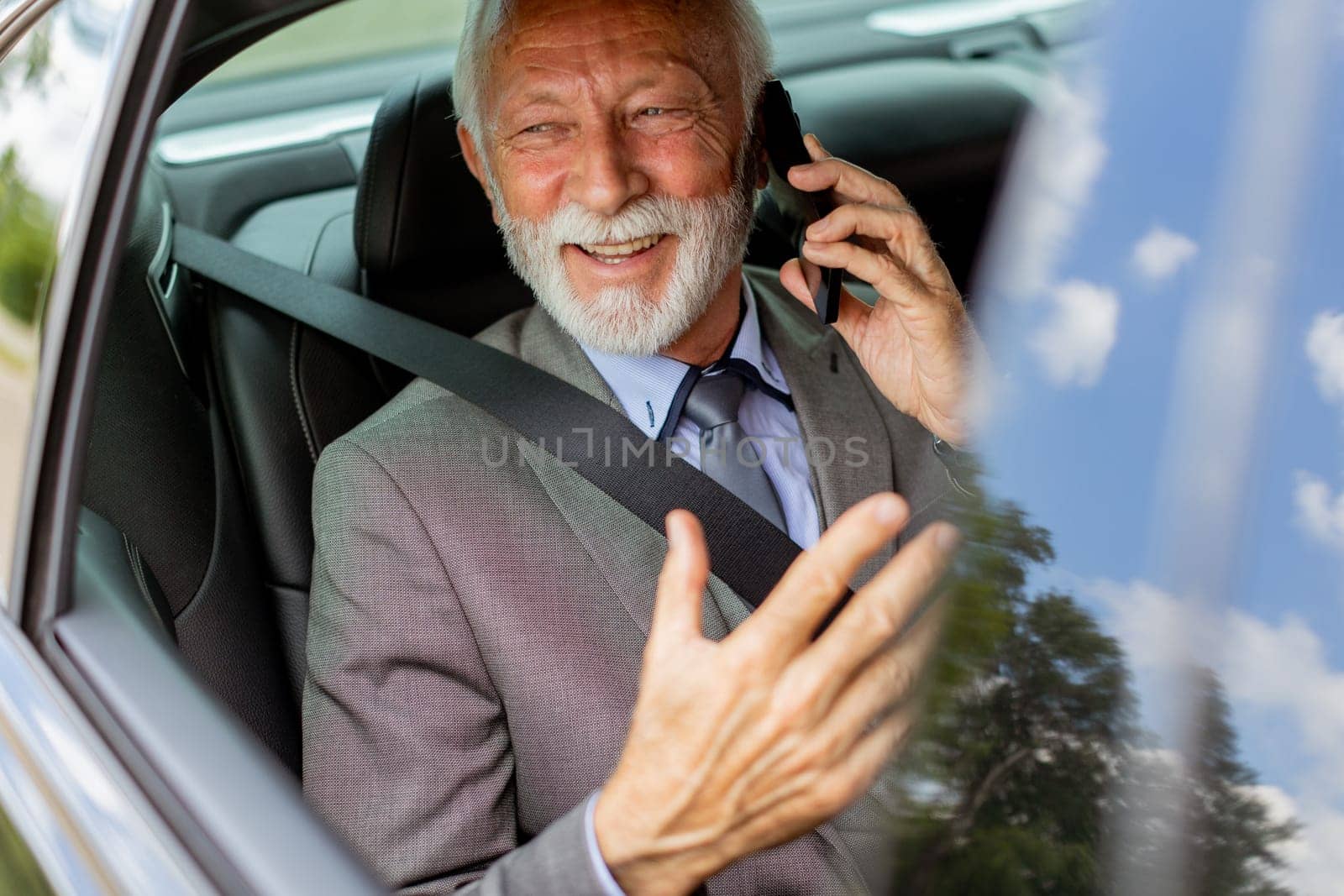 Suave senior man converses on his cell during a leisurely car ride, exuding charm and confidence