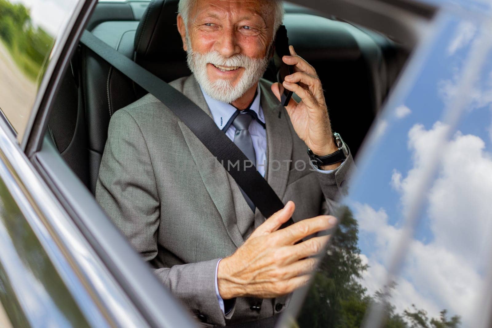 Suave senior man converses on his cell during a leisurely car ride, exuding charm and confidence