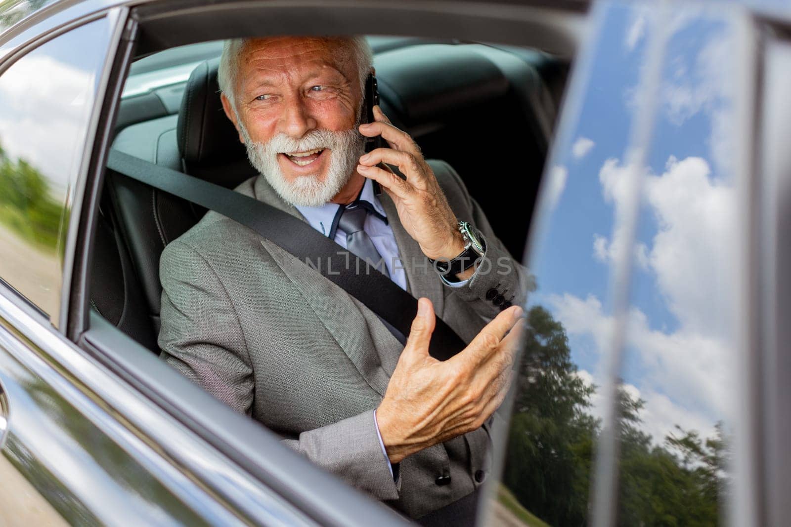 Suave senior man converses on his cell during a leisurely car ride, exuding charm and confidence