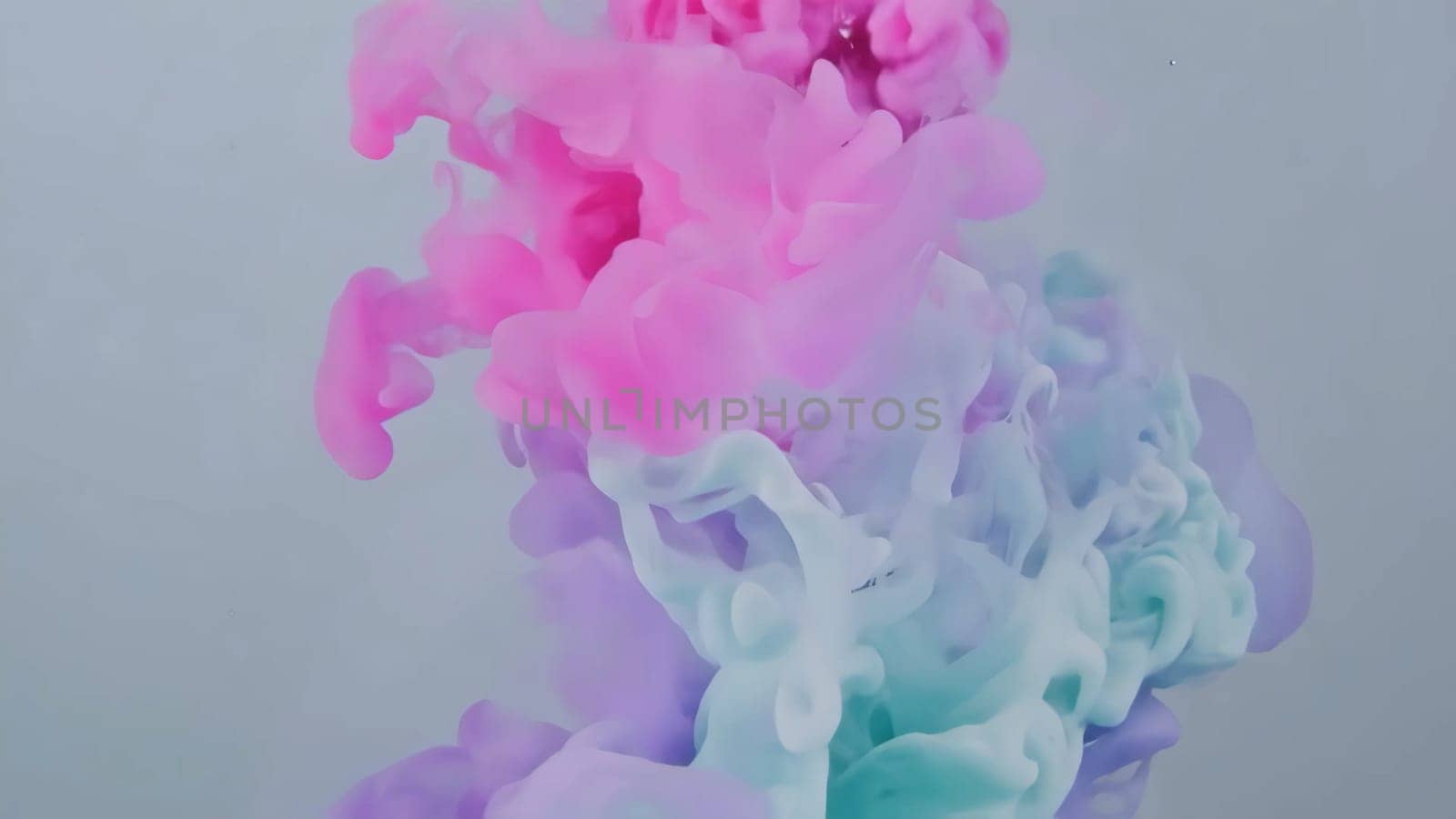 Colorful flowing ink moves gracefully across a soft backdrop, blending shades and creating an artistic display. The liquid paint dances and drips, forming an abstract texture that captivates the eye.