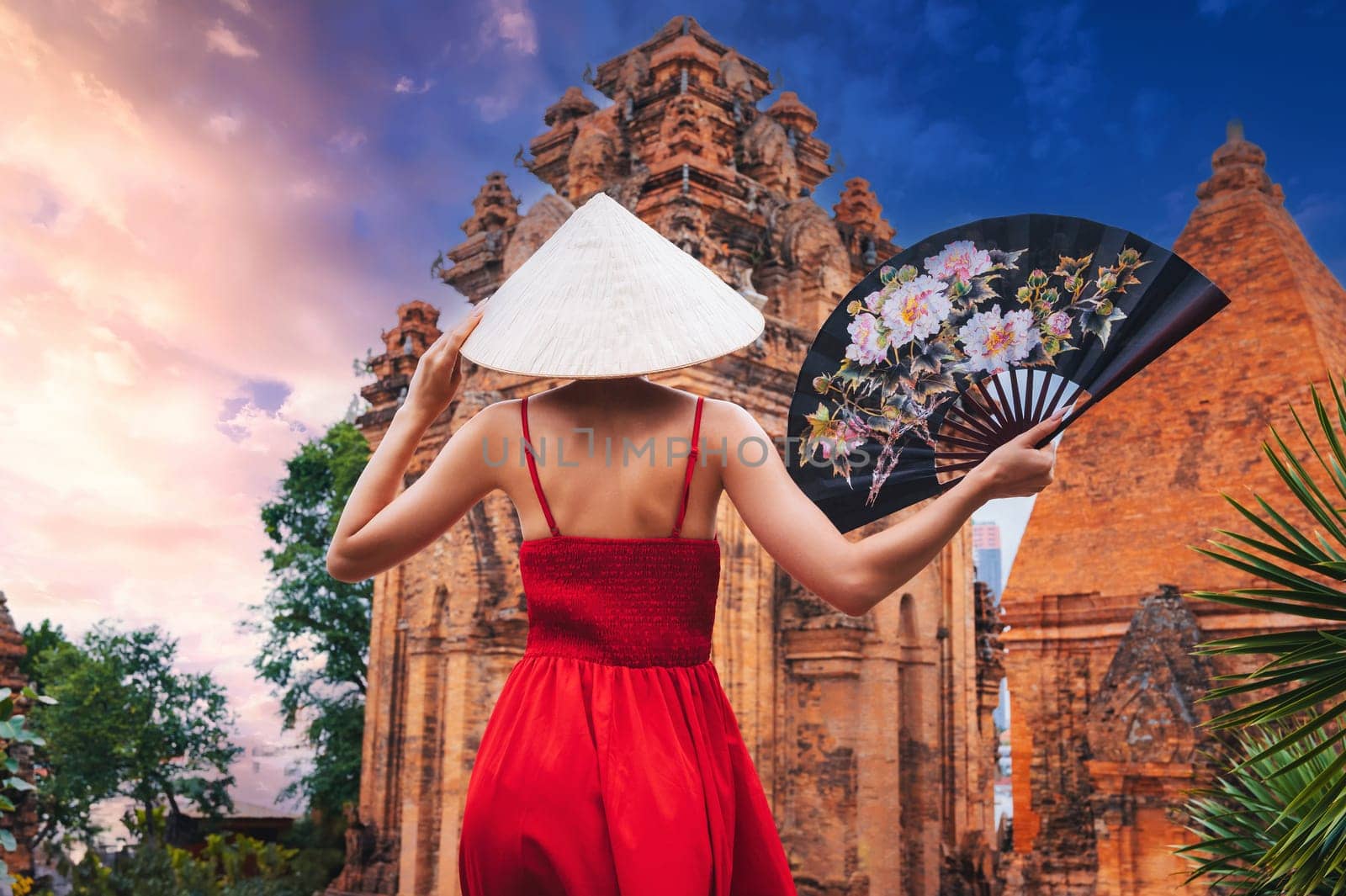 back of Asian girl tourist in Vietnamese hat Non La with fan on Cham Towers of Po Nagar in Nha Trang in Vietnam in Asia