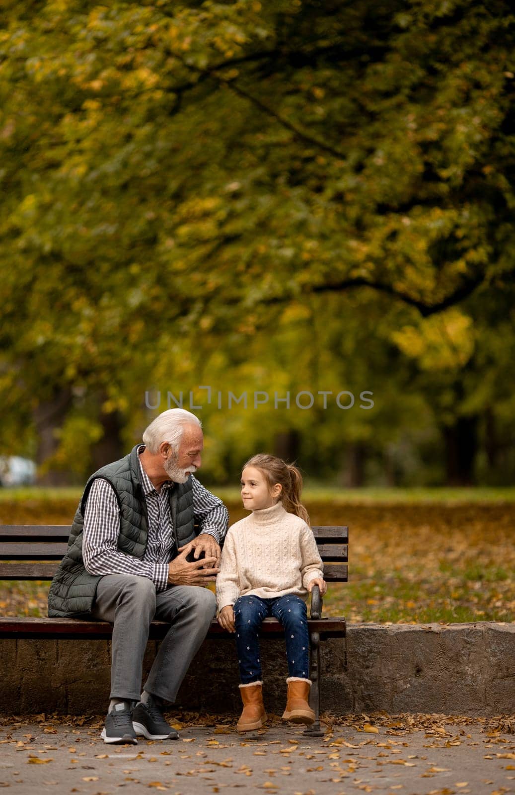 Handsome grandfather spending time with his granddaughter on bench in park on autumn day