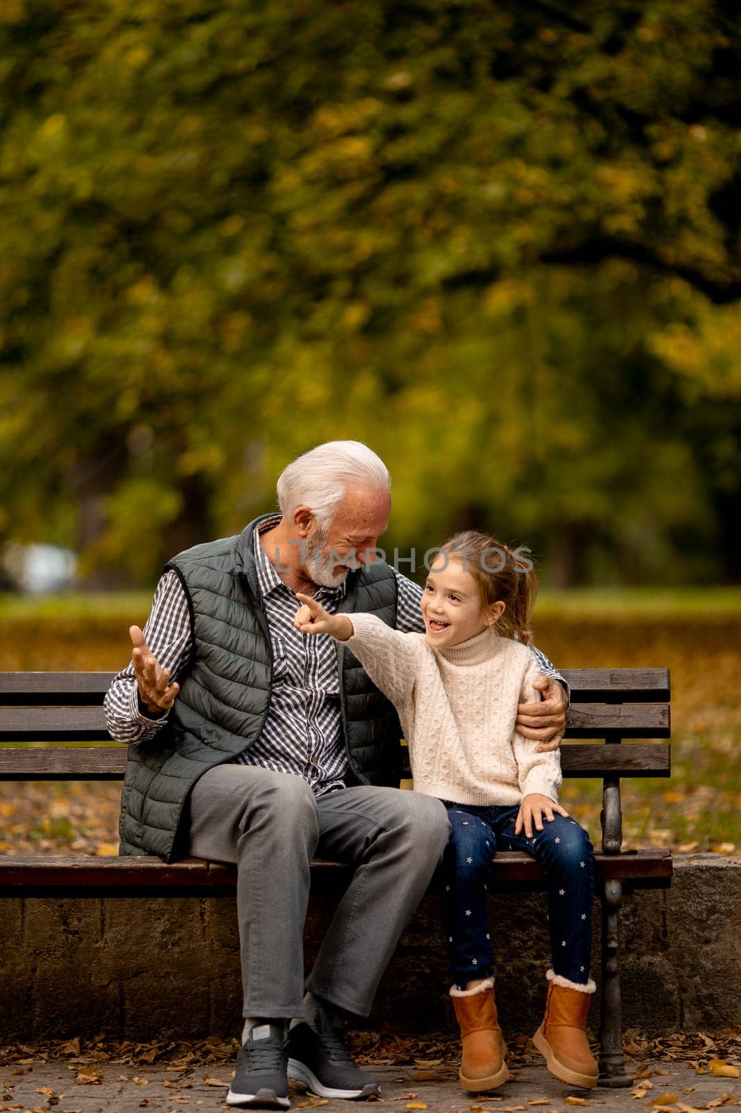 Handsome grandfather spending time with his granddaughter on bench in park on autumn day