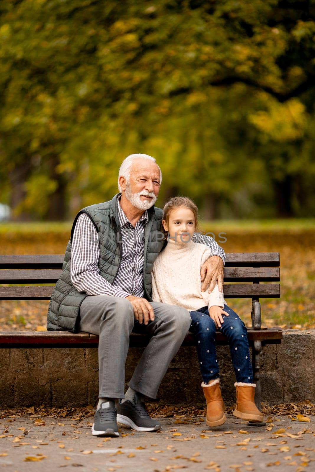 Handsome grandfather spending time with his granddaughter on bench in park on autumn day