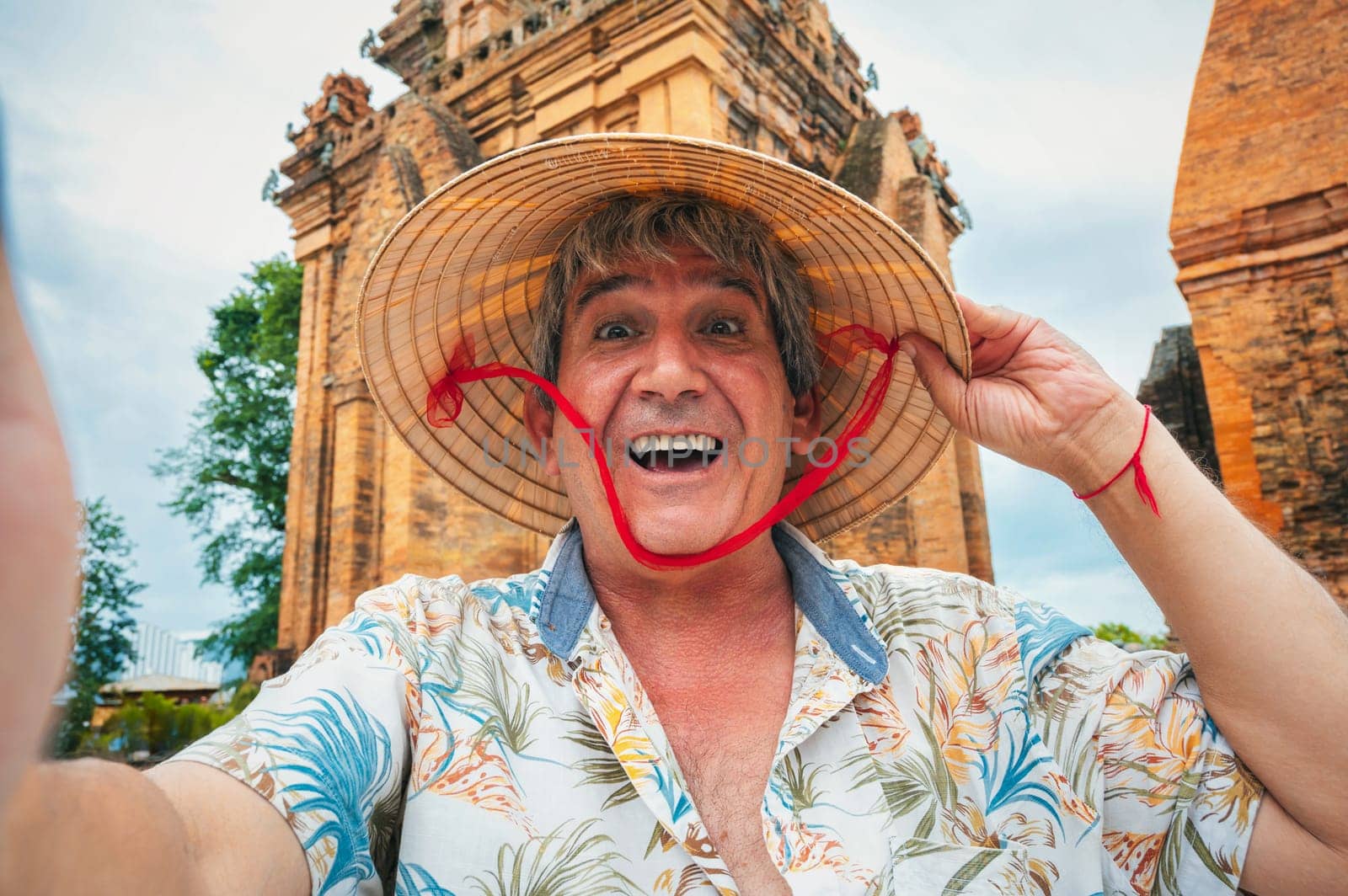 happy elderly male traveler in Vietnamese cone hat non la takes a selfie at the Po Nagar Cham Towers in Nha Trang, Vietnam. The concept of travel in Asia