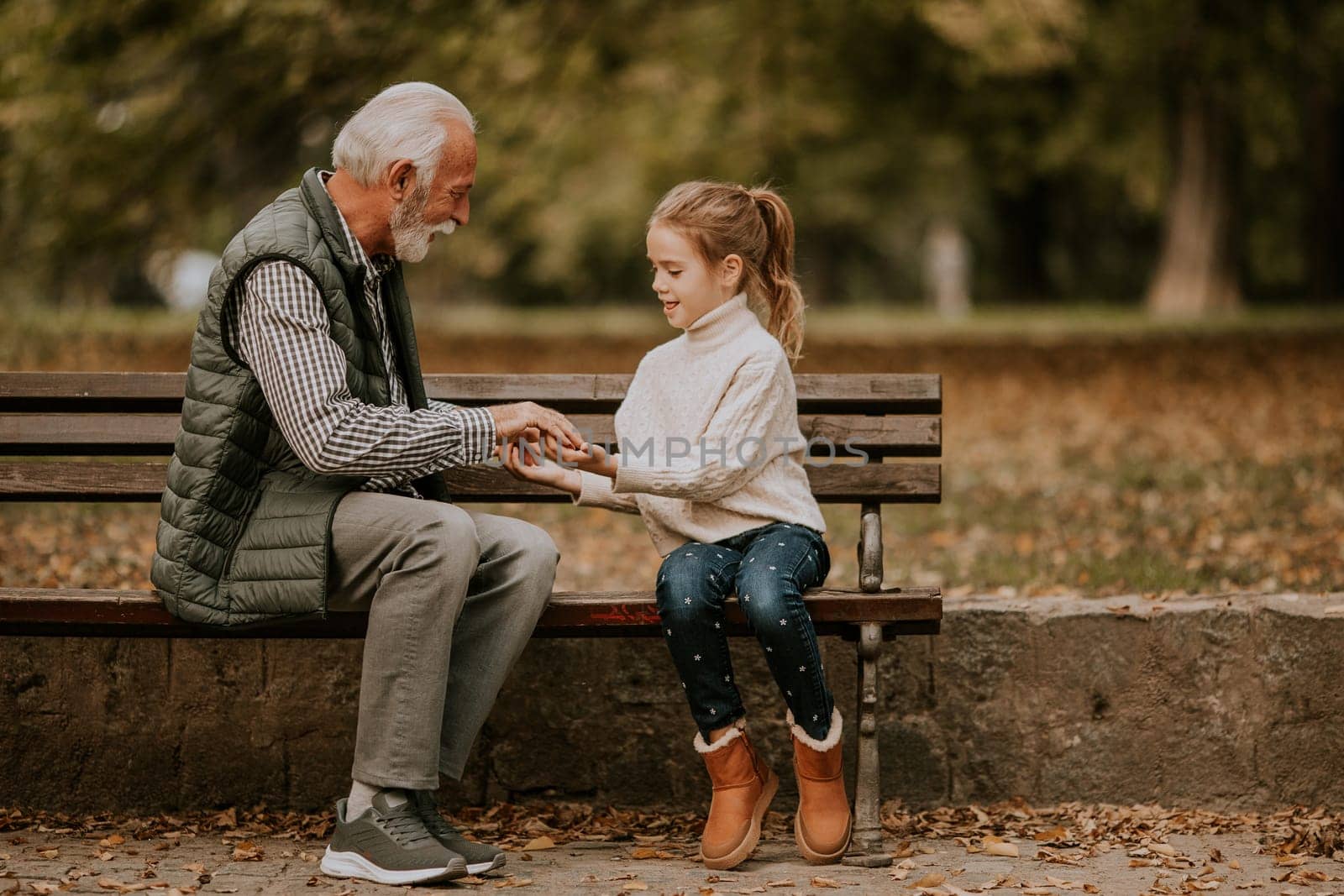 Handsome grandfather playing red hands slapping game with his granddaughter in park on autumn day