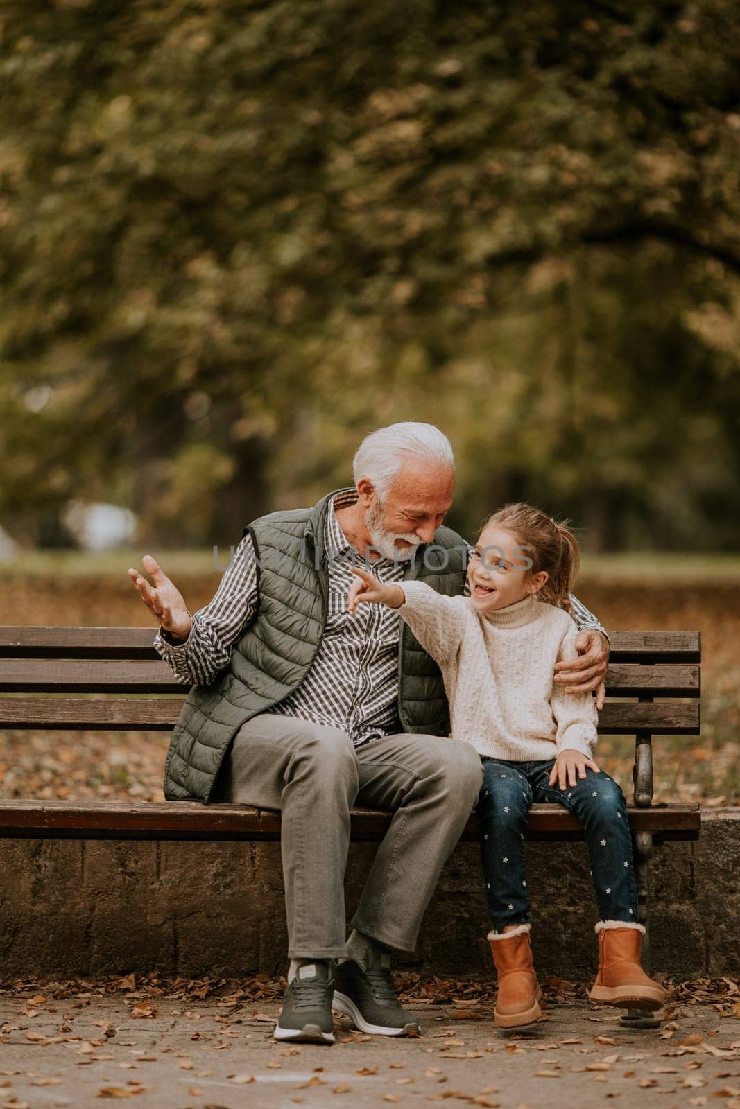 Handsome grandfather spending time with his granddaughter on bench in park on autumn day