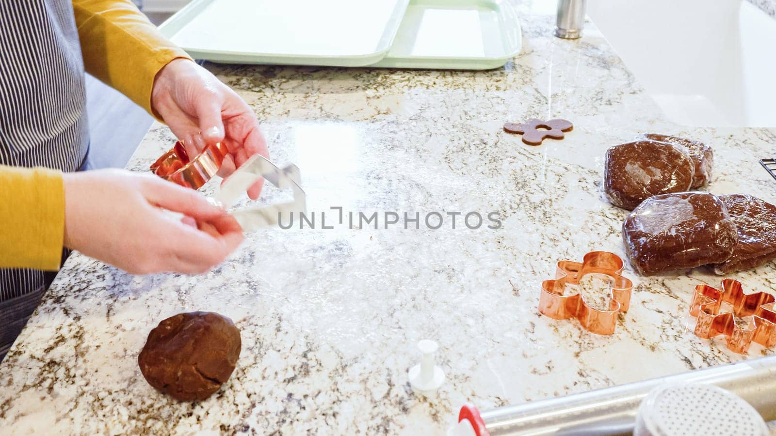 Using various festive cookie cutters, we're cutting out charming gingerbread cookies from the rolled dough on the sleek marble counter, bringing holiday cheer to the modern kitchen.