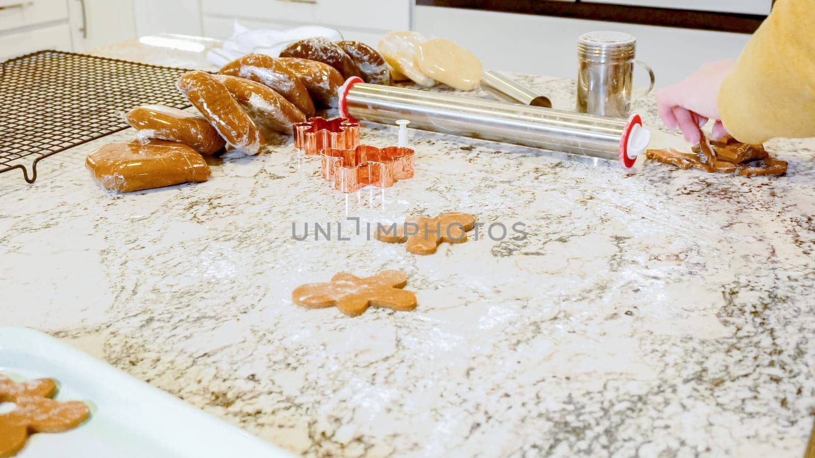 Using various festive cookie cutters, we're cutting out charming gingerbread cookies from the rolled dough on the sleek marble counter, bringing holiday cheer to the modern kitchen.