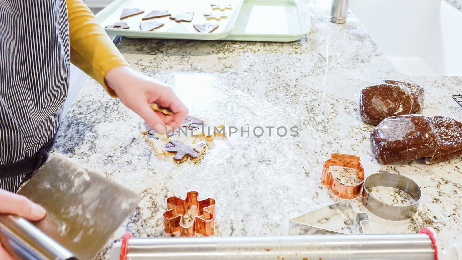 Using various festive cookie cutters, we're cutting out charming gingerbread cookies from the rolled dough on the sleek marble counter, bringing holiday cheer to the modern kitchen.
