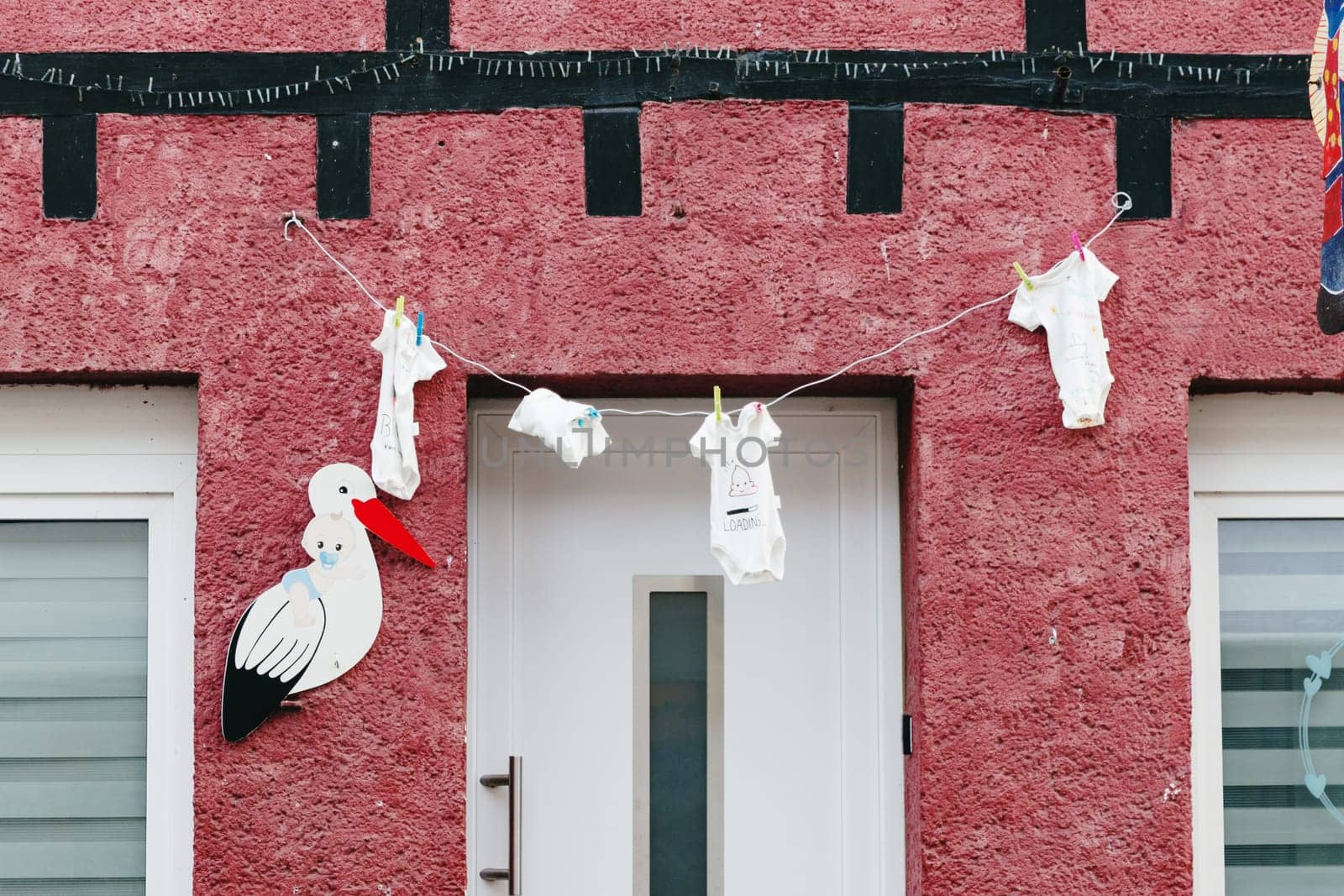 Beautiful view of baby clothes hanging on clothesline attached with clothespins and decorative stork figure in front of main door to house on spring day, side view medium shot. Concept street decor, national customs, travel time and tourism.