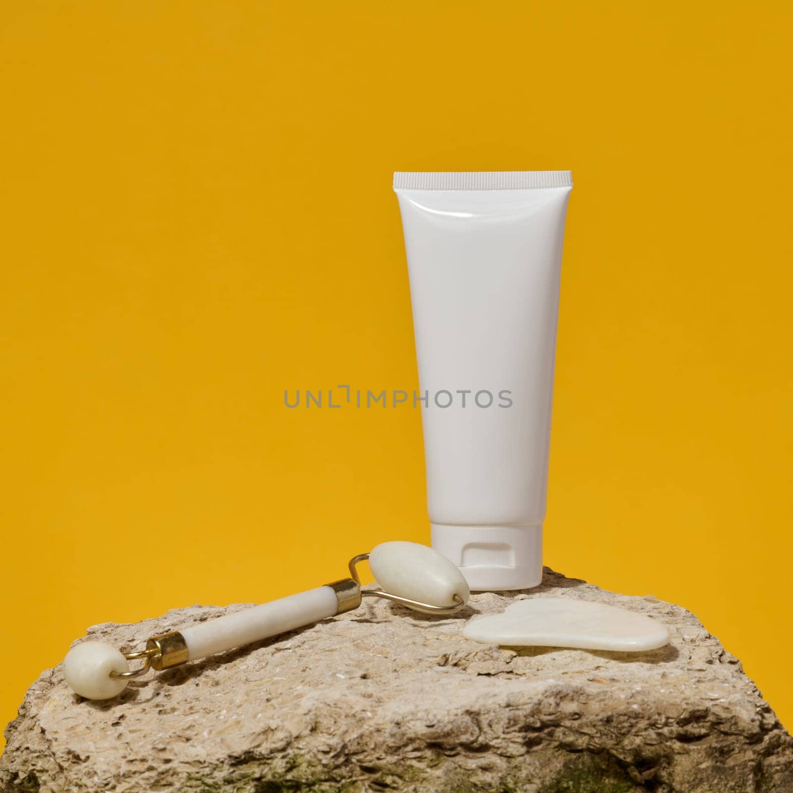White tube, jade gouache massager and massage jade roller on a yellow background