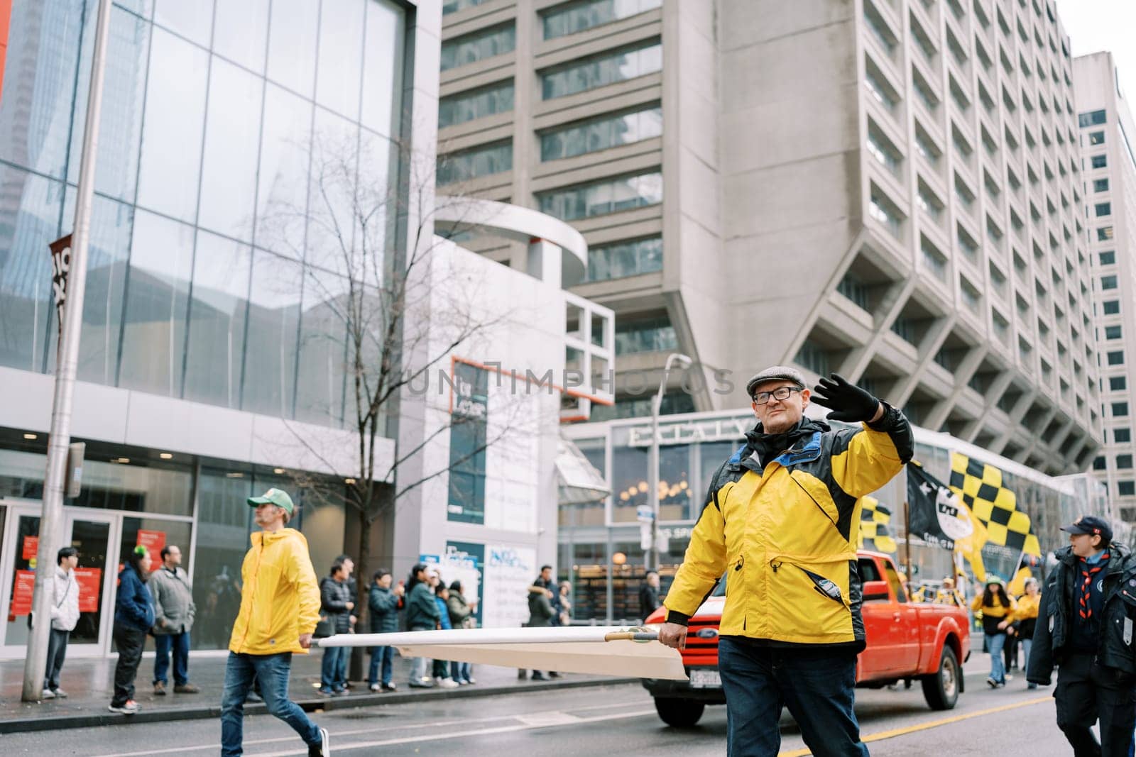 Participants in bright yellow jackets joyfully walk in a lively city parade