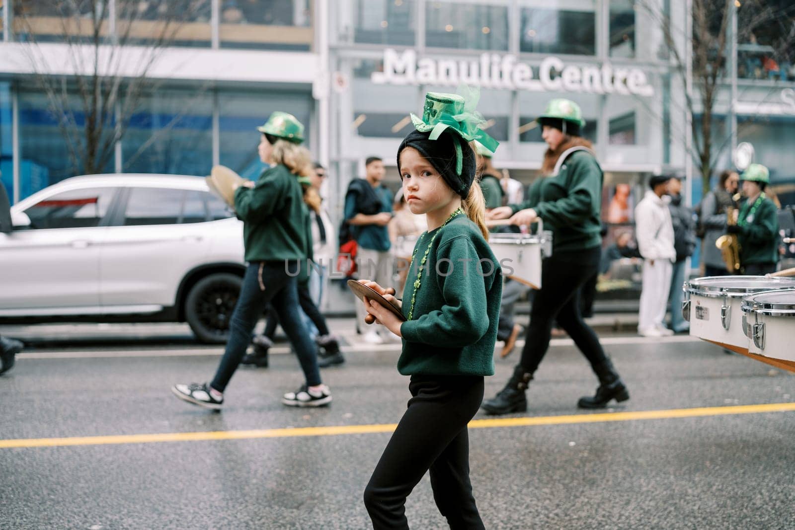 A group of young performers in green outfits joyfully join a lively parade