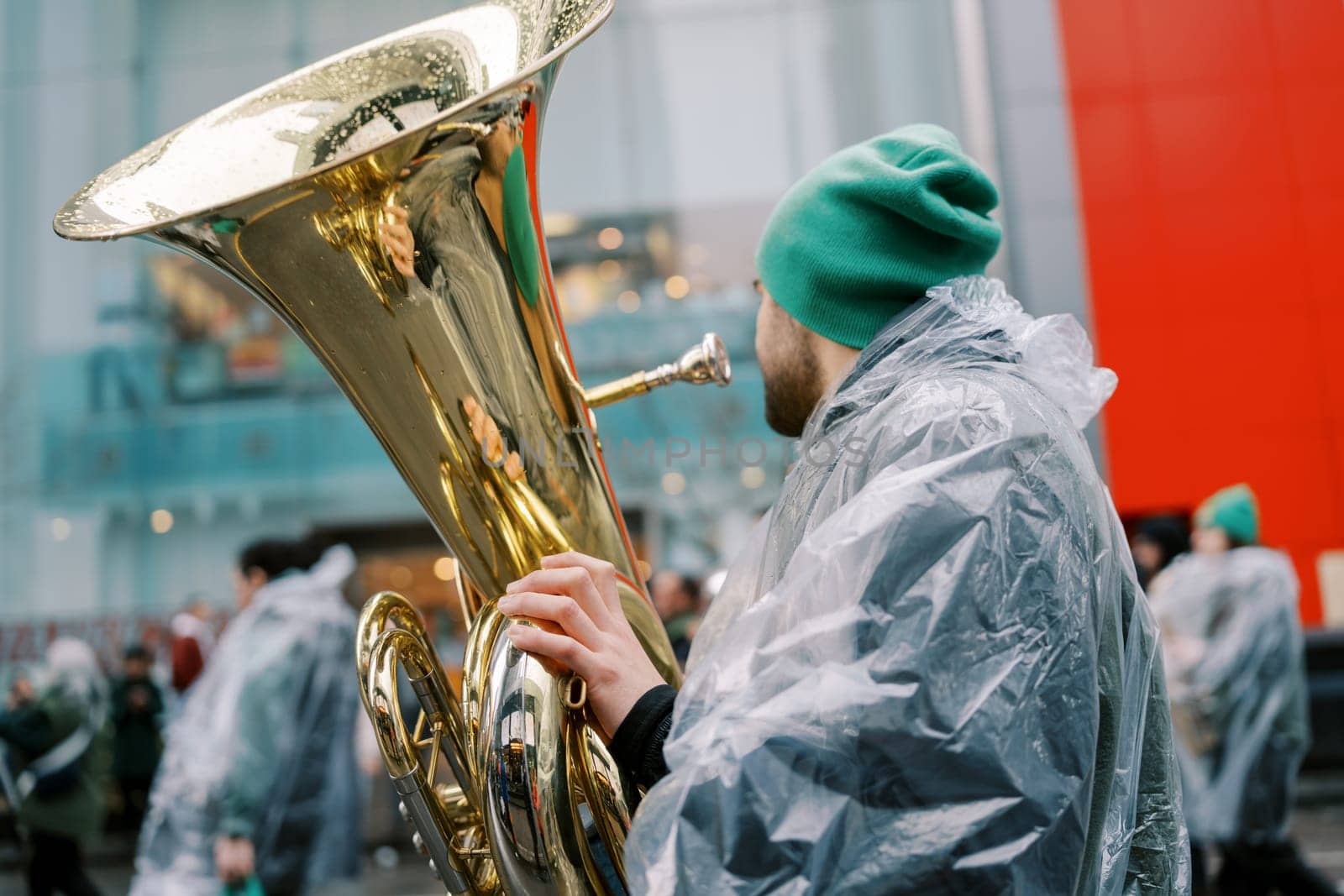 A musician is playing a tuba while wearing a rain poncho at a lively festive gathering
