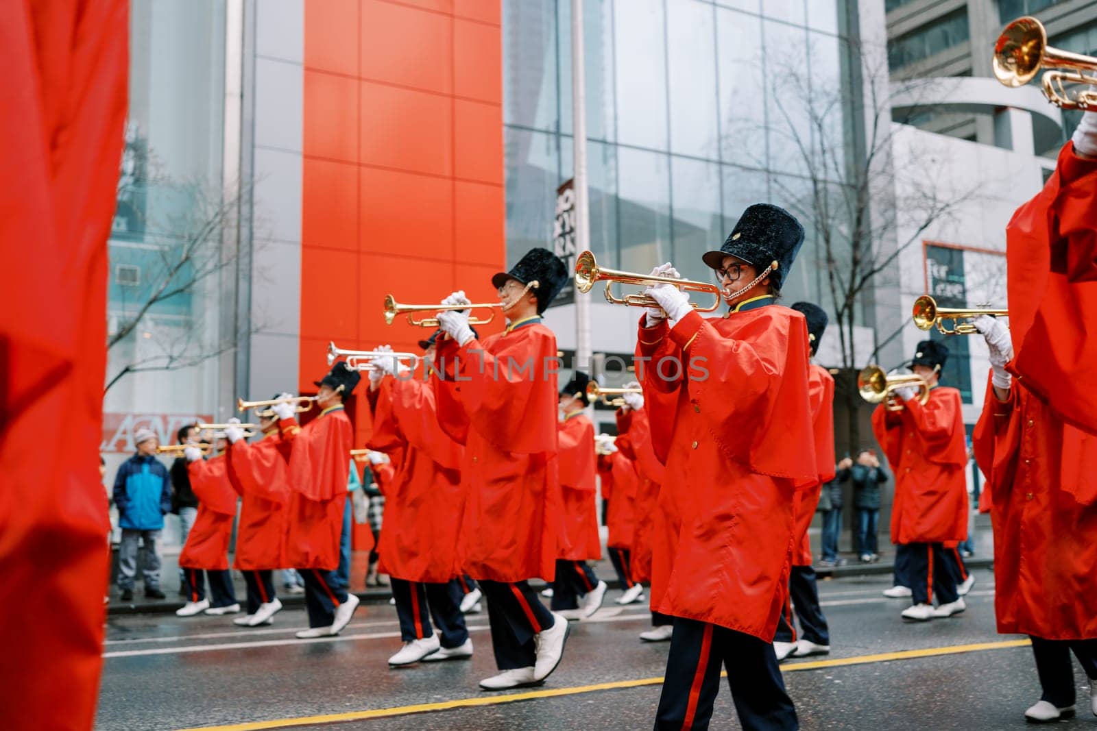 A vibrant parade scene with musicians dressed in red raincoats playing trumpets.