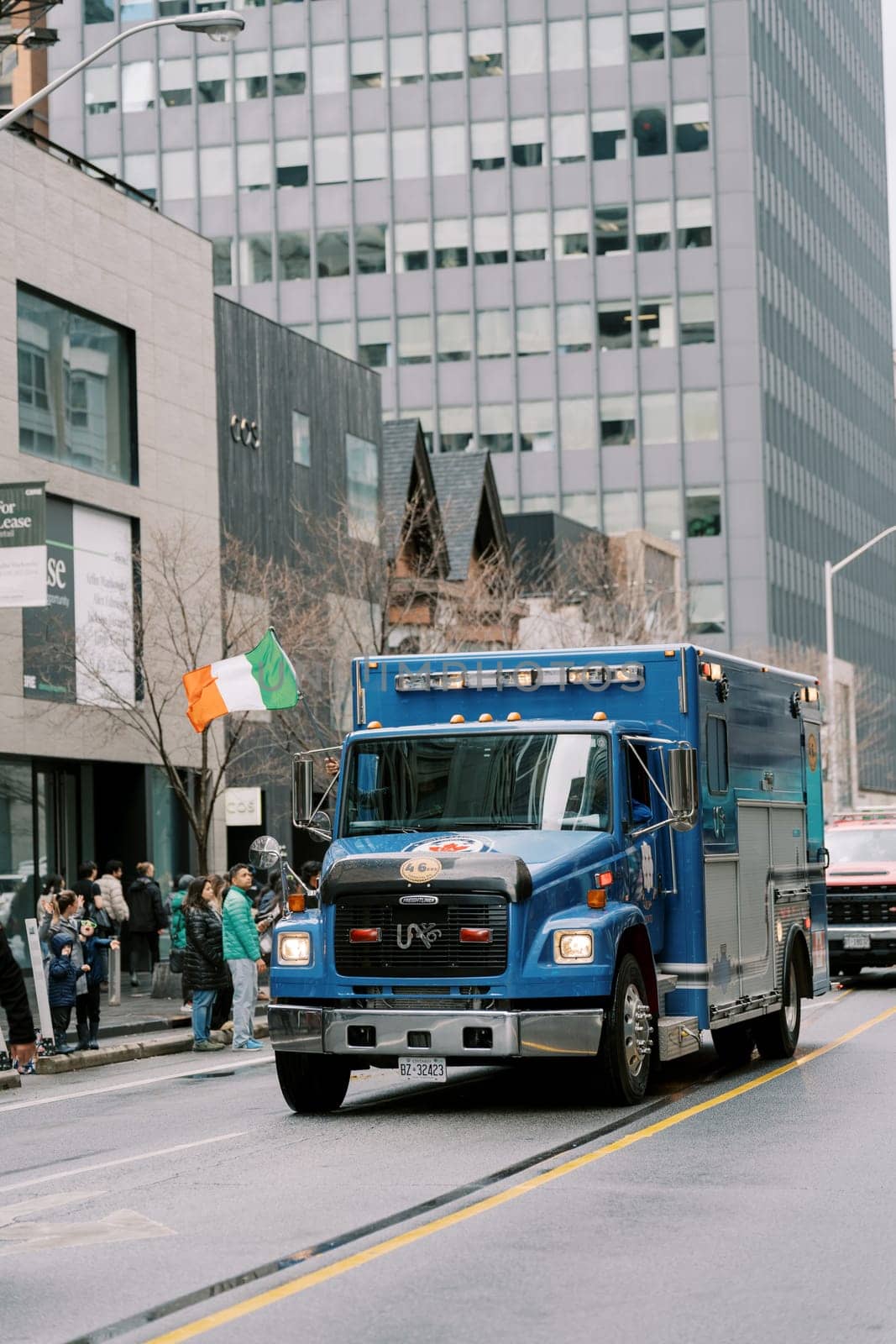 A blue ambulance rushes past crowds and tall buildings, creating urgency and excitement